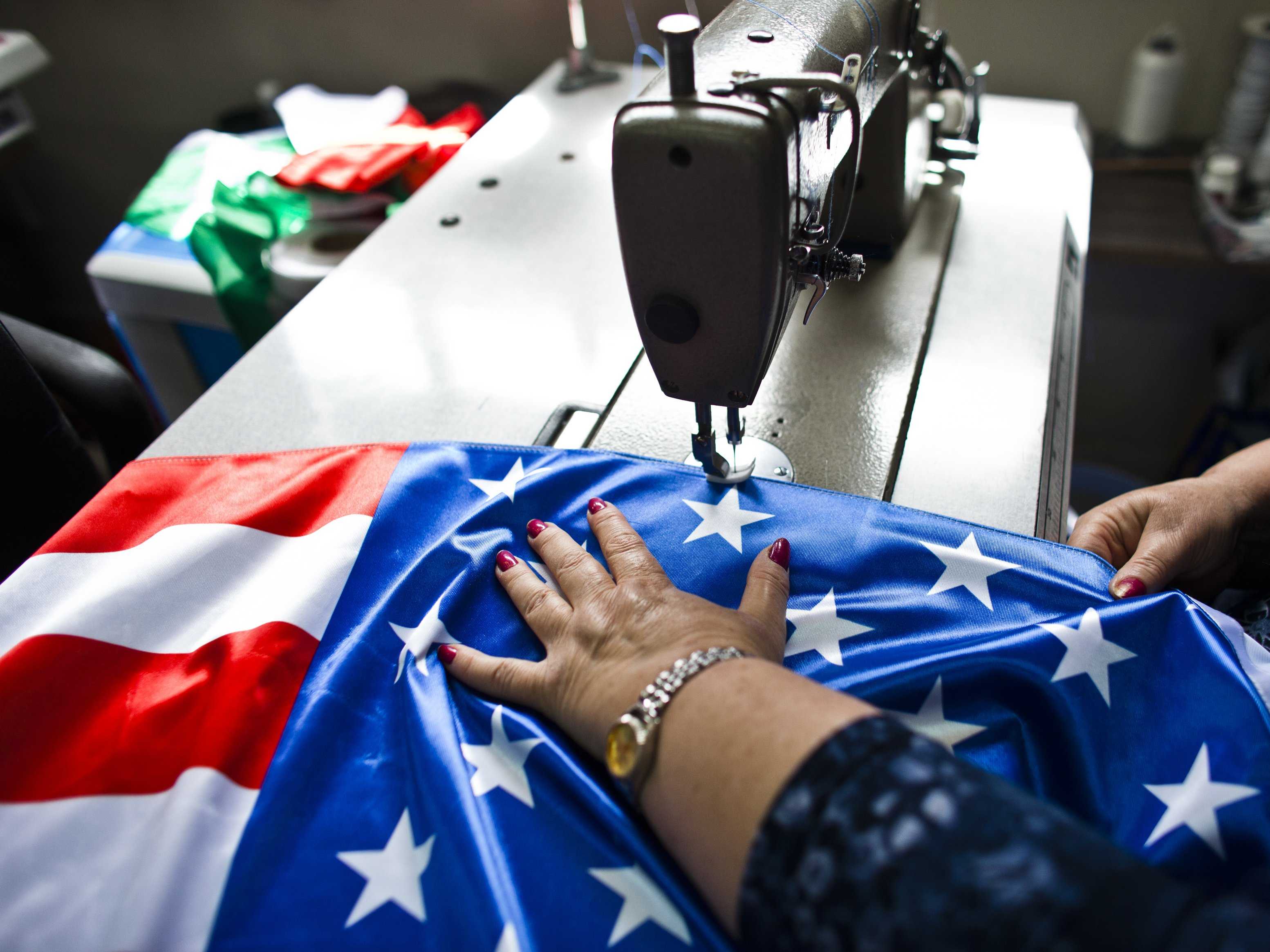 A woman sewing an American flag in a factory, symbolizing manufacturing and labor contributing to the US economy and job market.