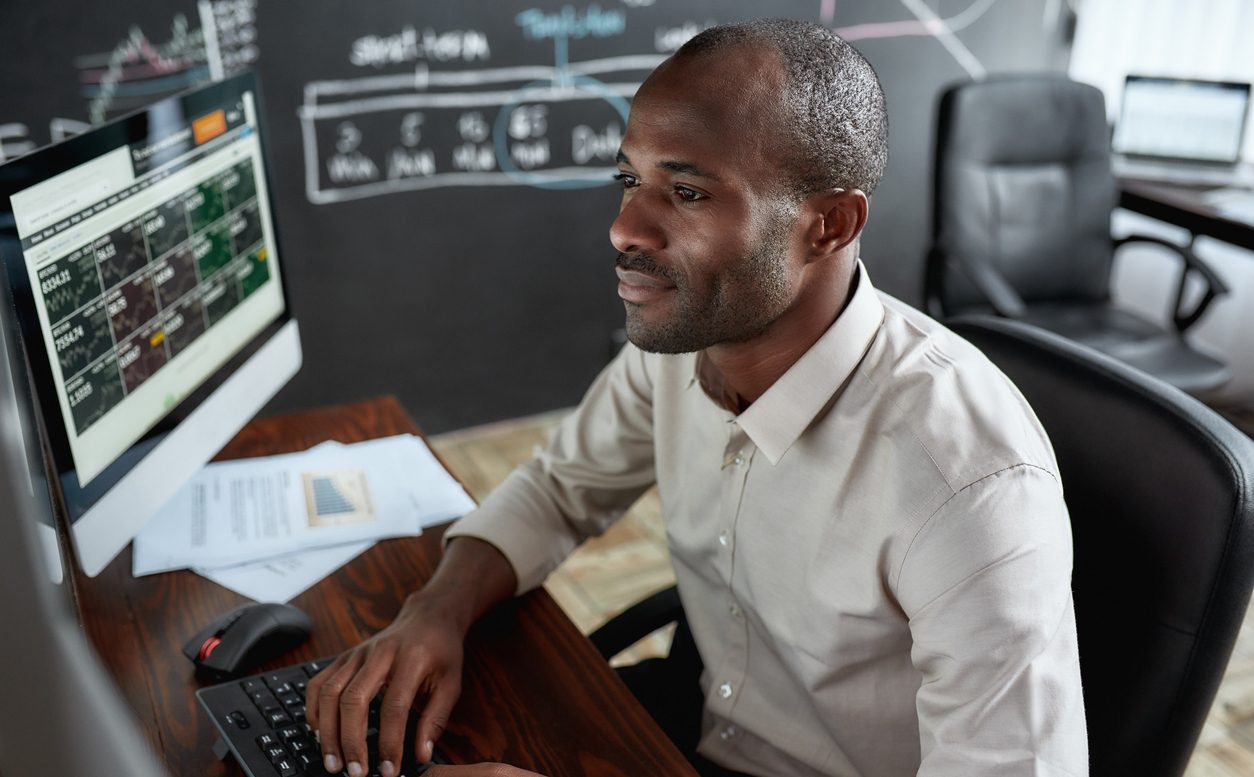 Young African trader reading stock reports in office