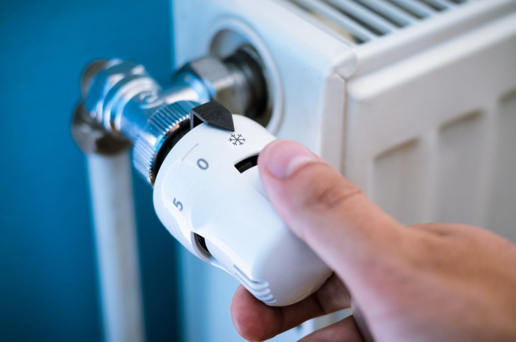 Hand turning down thermostat to save on rising energy costs