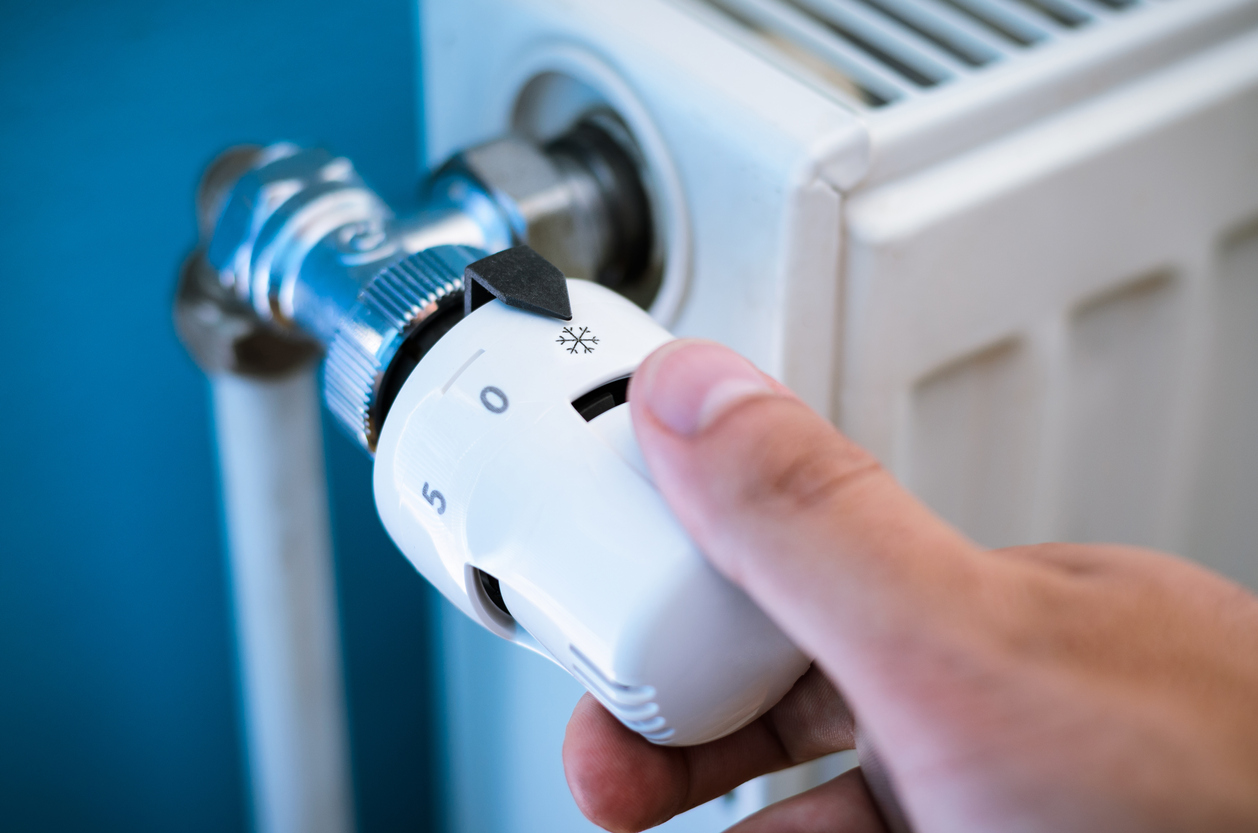 Hand turning down thermostat to save on rising energy costs