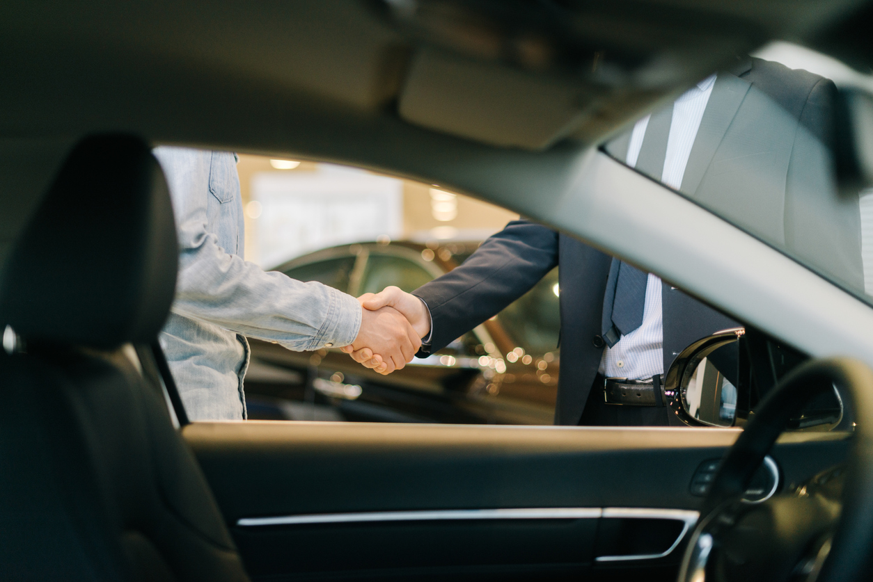 Buyer of car shaking hands with seller in auto dealership, view from interior of car
