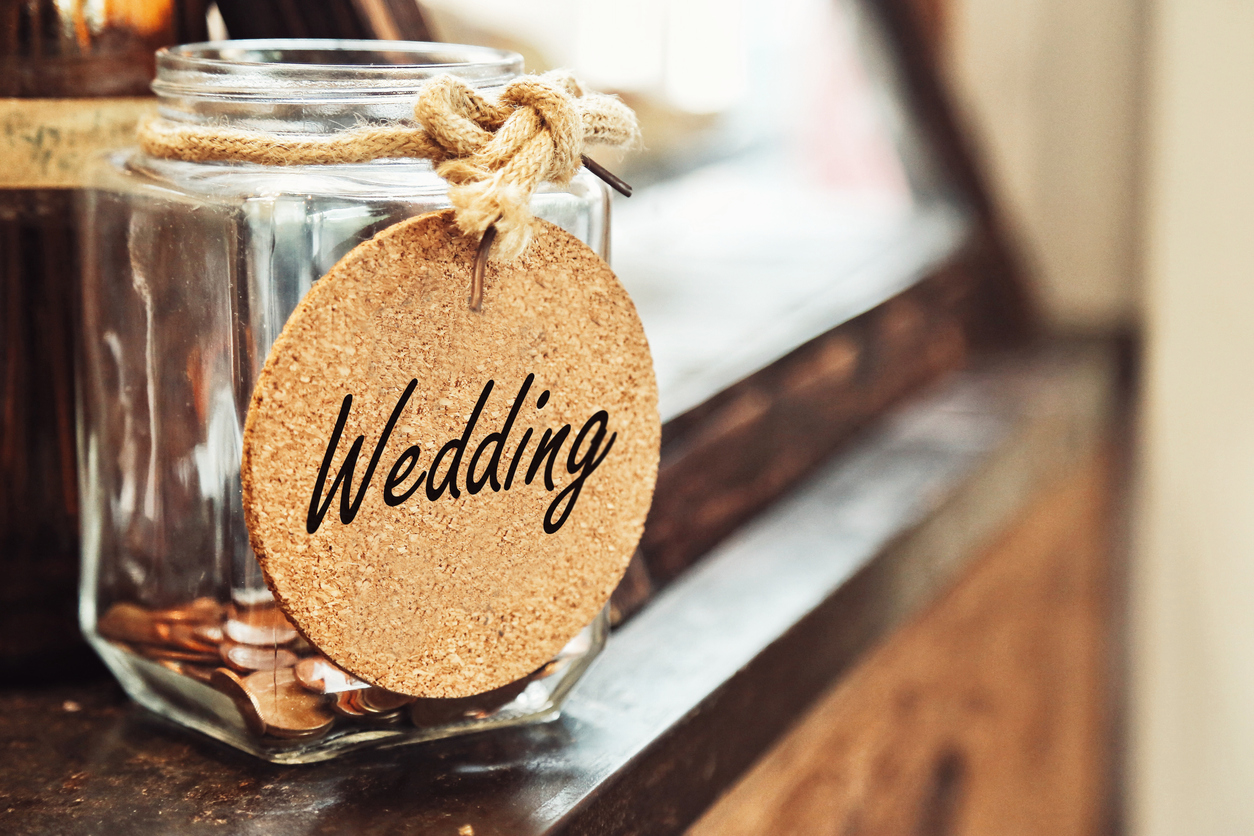 Vintage retro glass jar with hemp rope tie wedding tag and few coins inside on wood counter concept of saving money for wedding