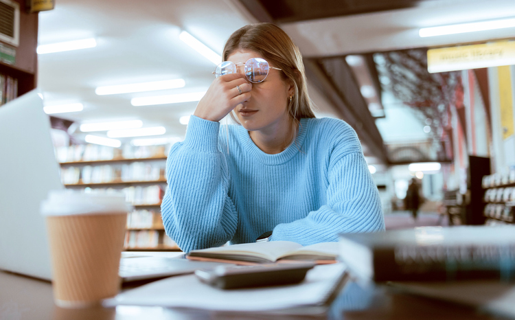 woman student, fatigue with headache and university burnout, stress for paper deadline or study for exam in library. campus, college and tired studying with scholarship problem and mental health pain