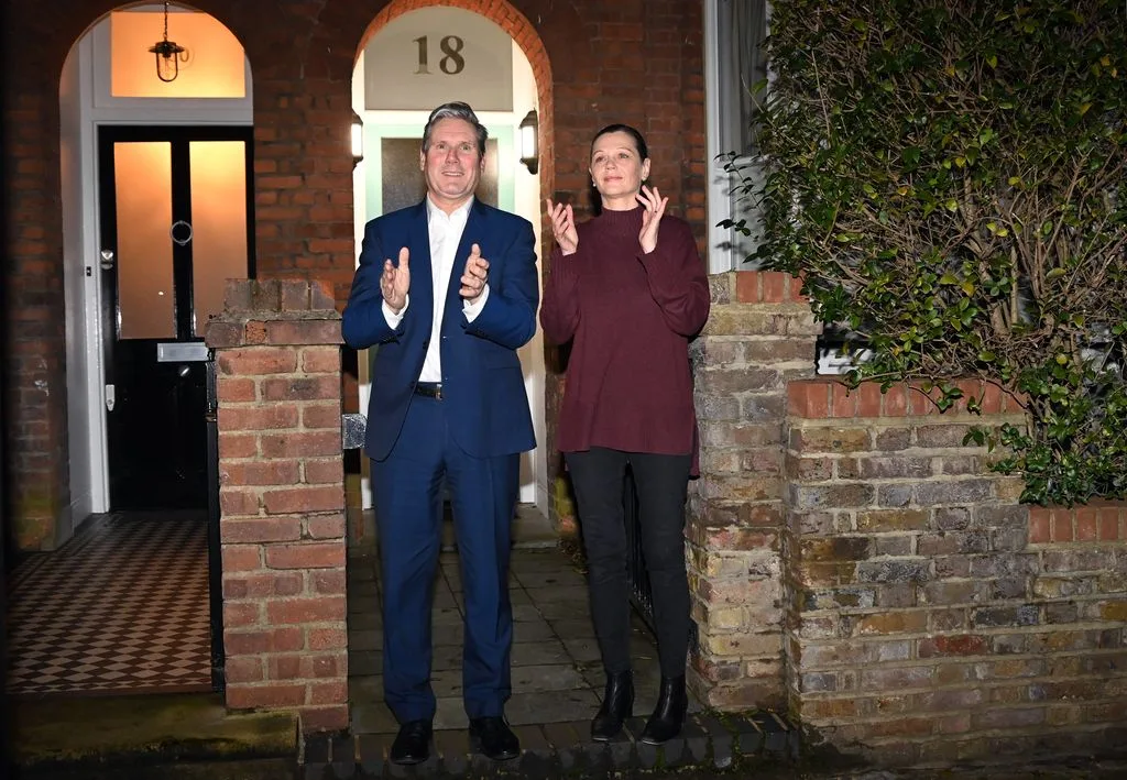“Keir Starmer and his wife Victoria standing outside their North London home, dressed smartly, smiling for the camera.
