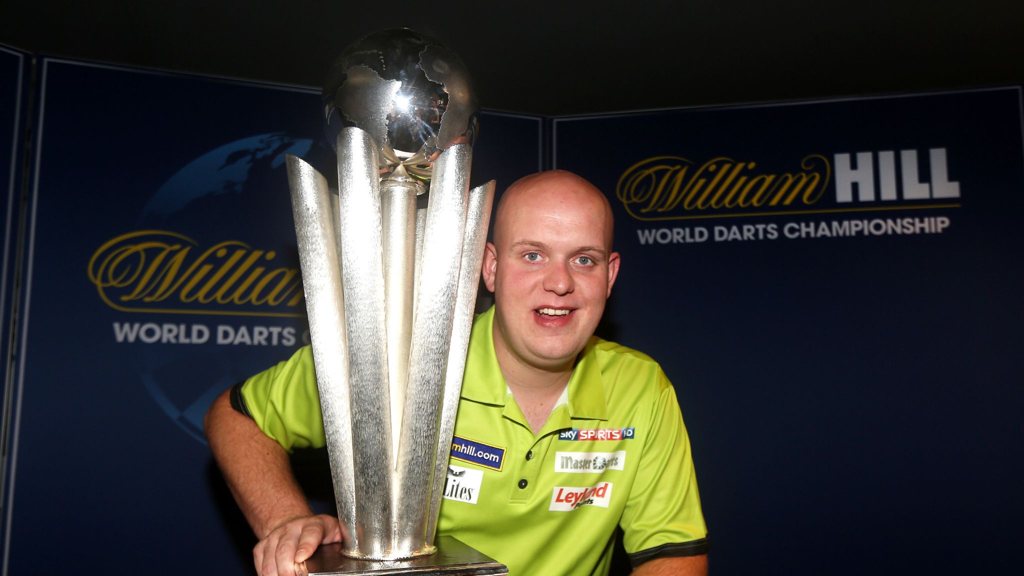 Michael van Gerwen holding the Sid Waddell Trophy triumphantly, smiling after a major darts victory.