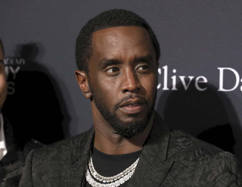 Close-up photo of Sean "Diddy" Combs wearing a patterned dark jacket and multiple diamond necklaces, looking thoughtfully to the side against a dark backdrop with white text.