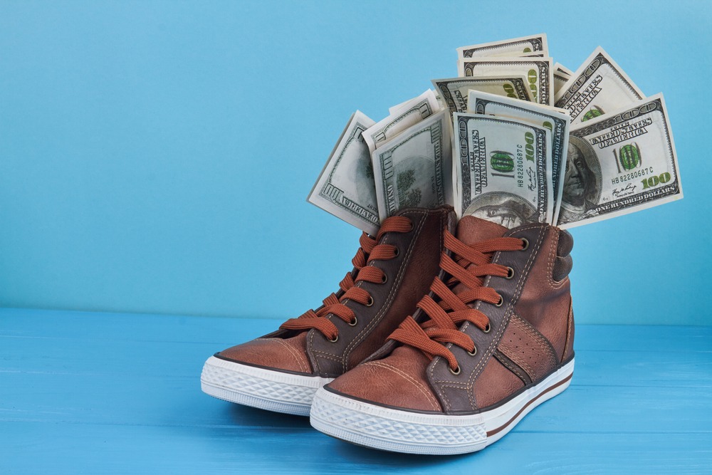 sneakers,shoes,with,dollar,banknotes.,blue,wooden,table.