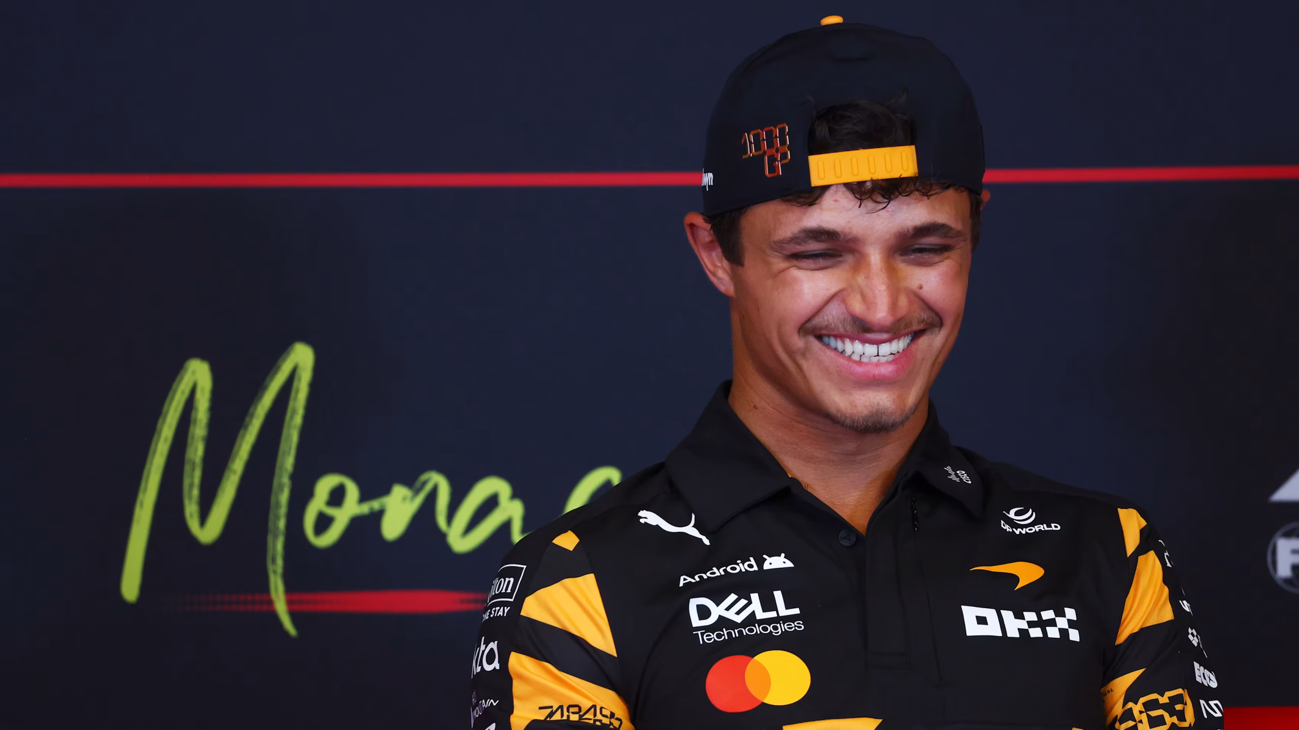 Lando Norris smiles during media duties at the 2026 Monaco Grand Prix wearing McLaren team apparel and a backwards cap.