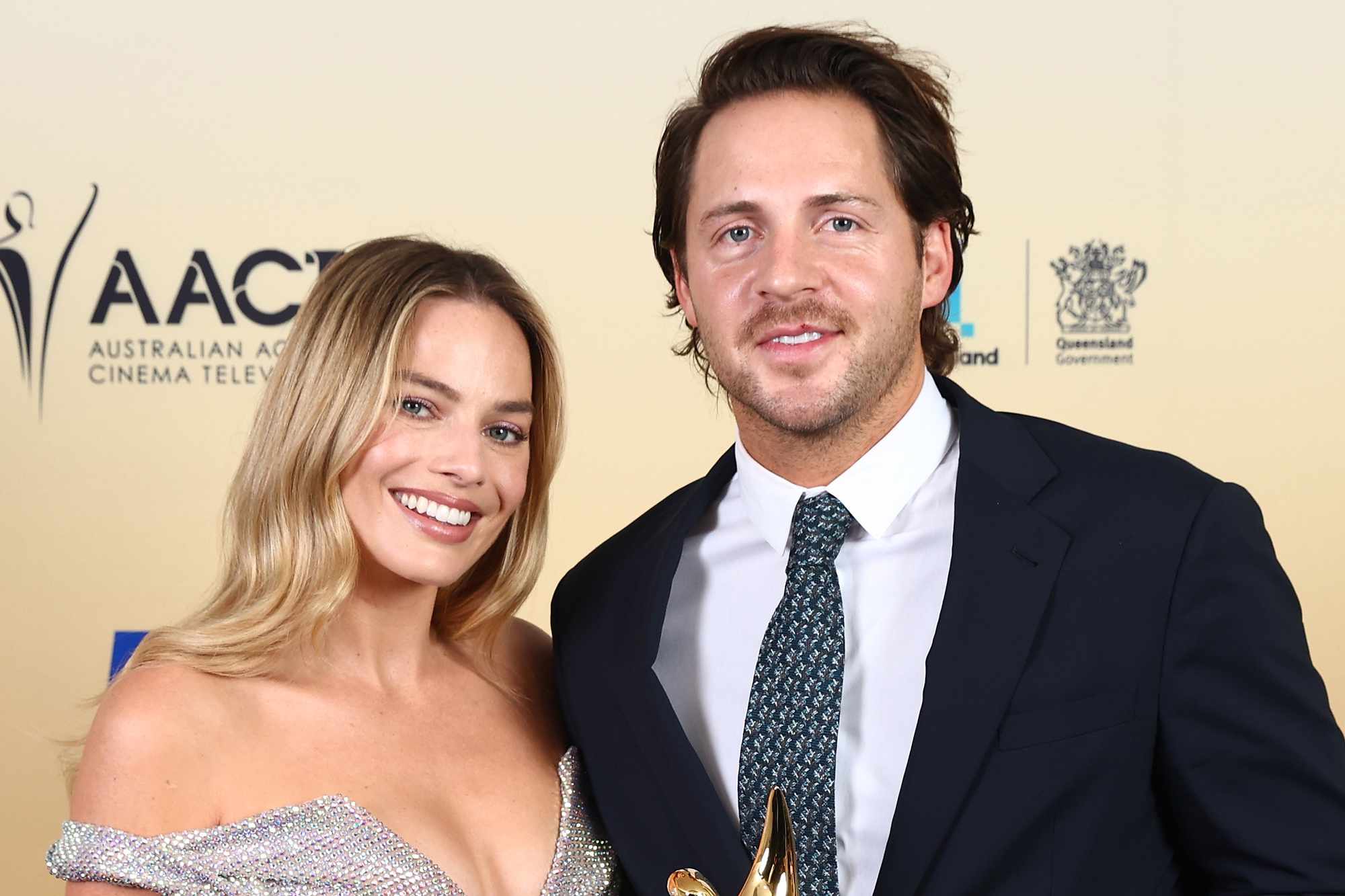 Margot Robbie and her husband Tom Ackerley smiling together on the red carpet at a film premiere.