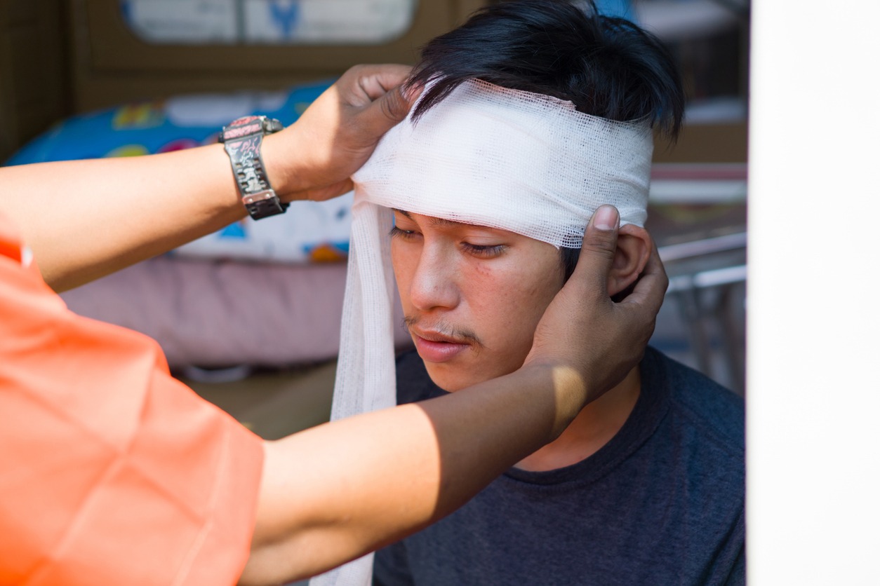 an accident victim man receiving medical attention, a bandage wrapped around his head from a medical professional. he's being treated for a minor head injury. on site emergency response situation.