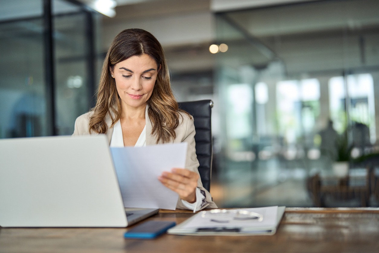 busy mid aged business woman working in office with laptop and documents.