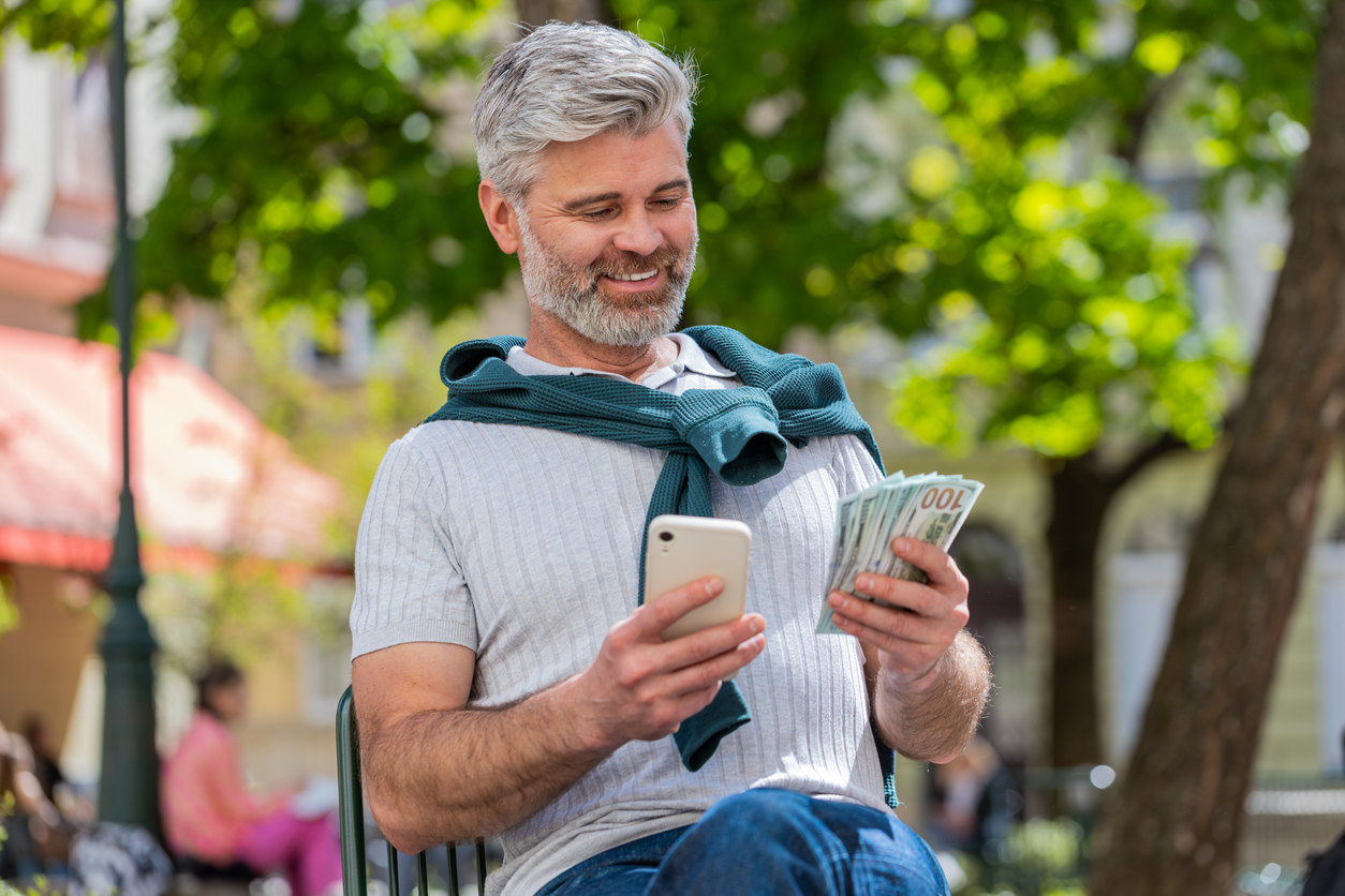 happy rich mature man counting holding money dollar cash use smartphone calculator app booking hotel