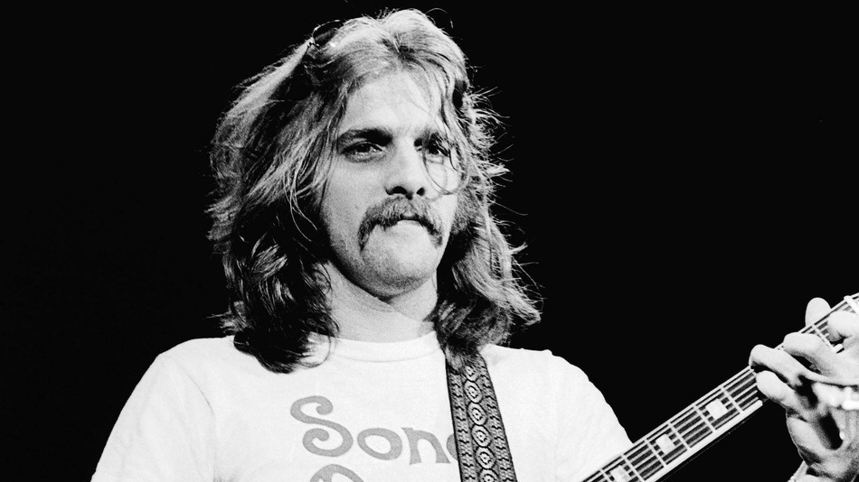 Black and white photo of a young Glenn Frey passionately performing on stage, playing guitar and singing during the early days of the Eagles.