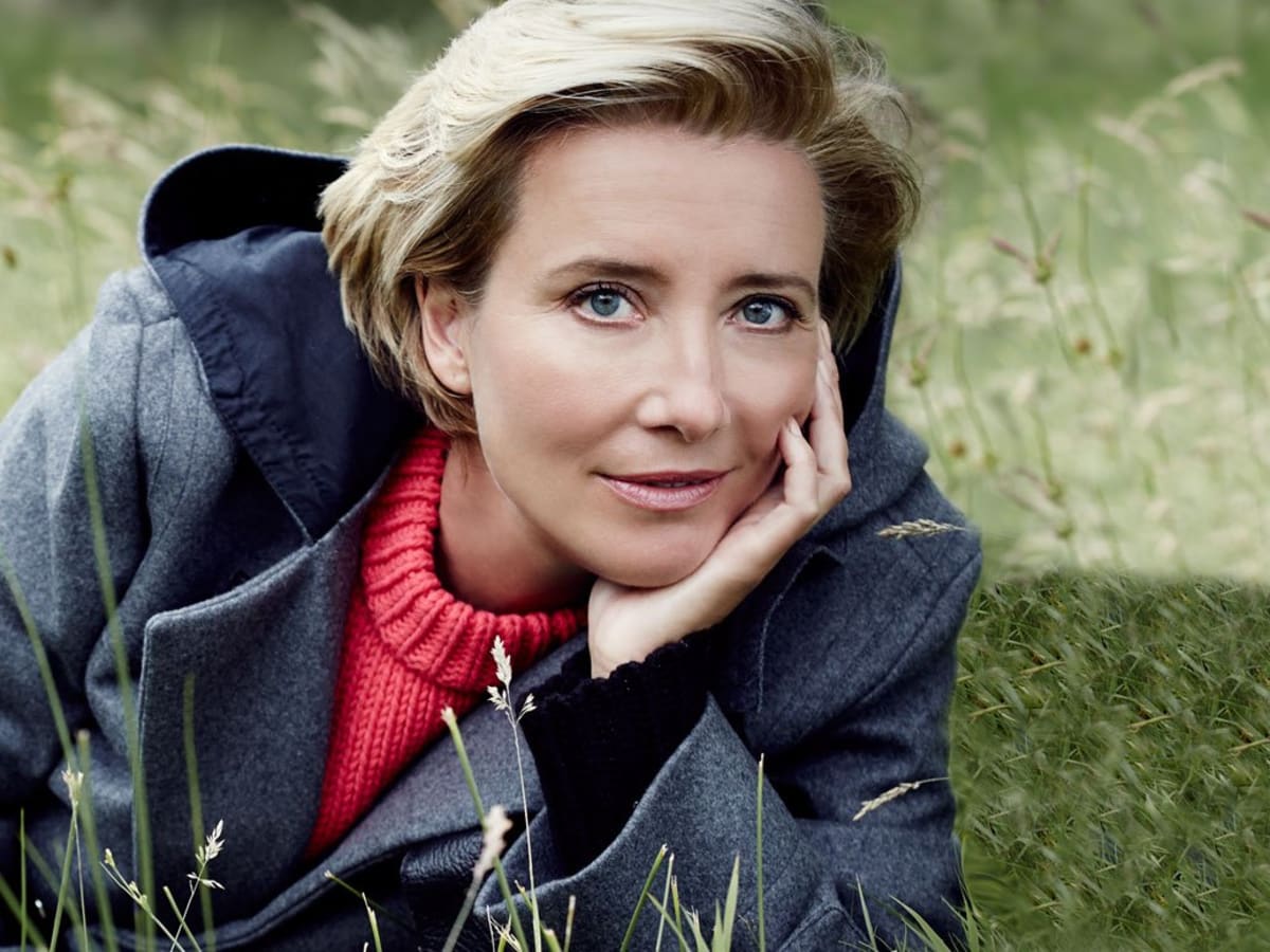 Young Emma Thompson posing outdoors in the grass, wearing a coat and looking thoughtfully into the distance.