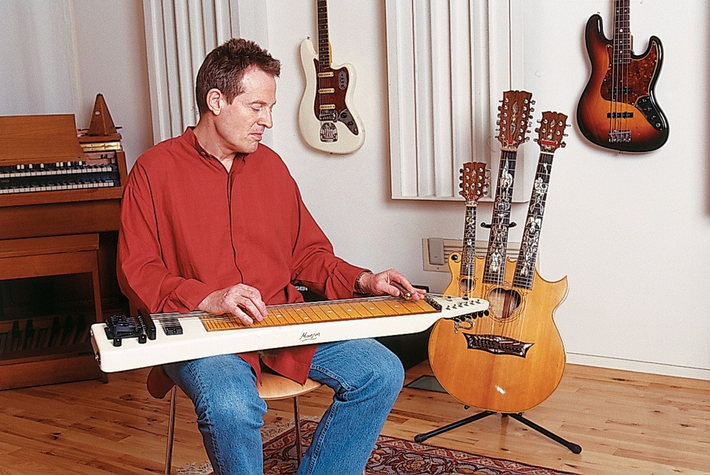 John Paul Jones adjusting his instrument during an interview, surrounded by cables and vintage gear.
