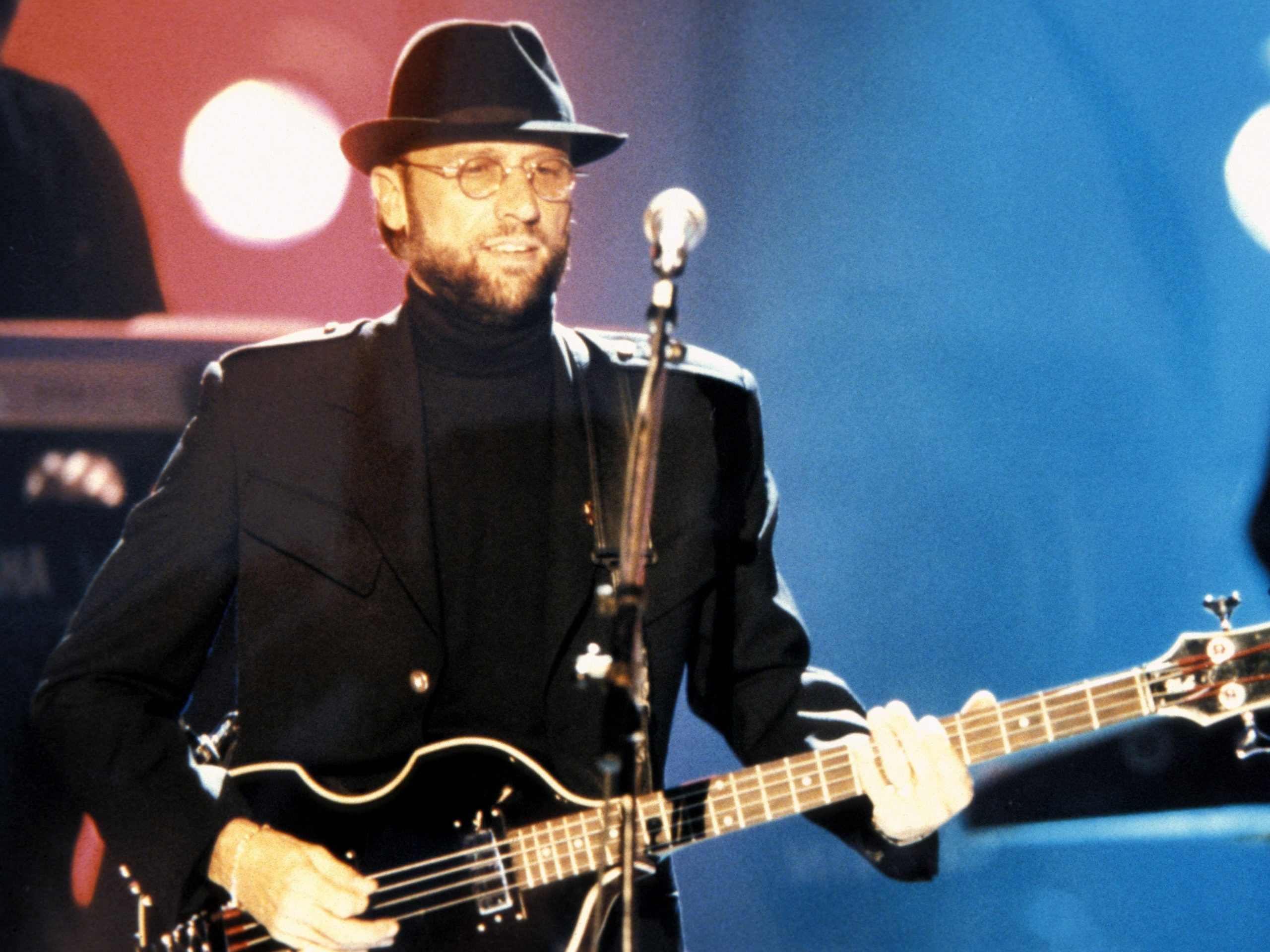 Maurice Gibb performing passionately on stage, playing guitar under vibrant stage lights.