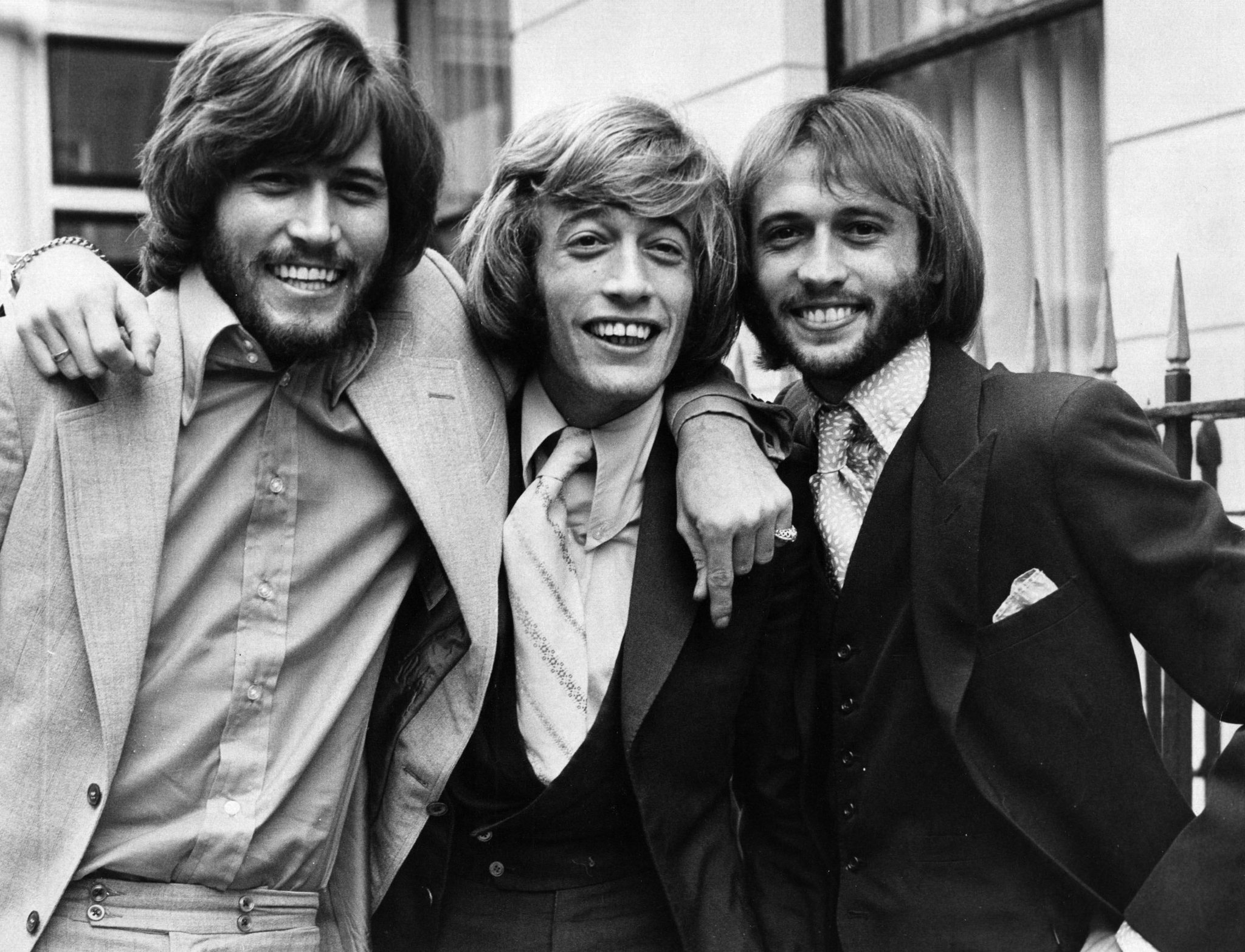A black and white photo of the young Bee Gees brothers posing together, smiling and embracing in a candid moment.