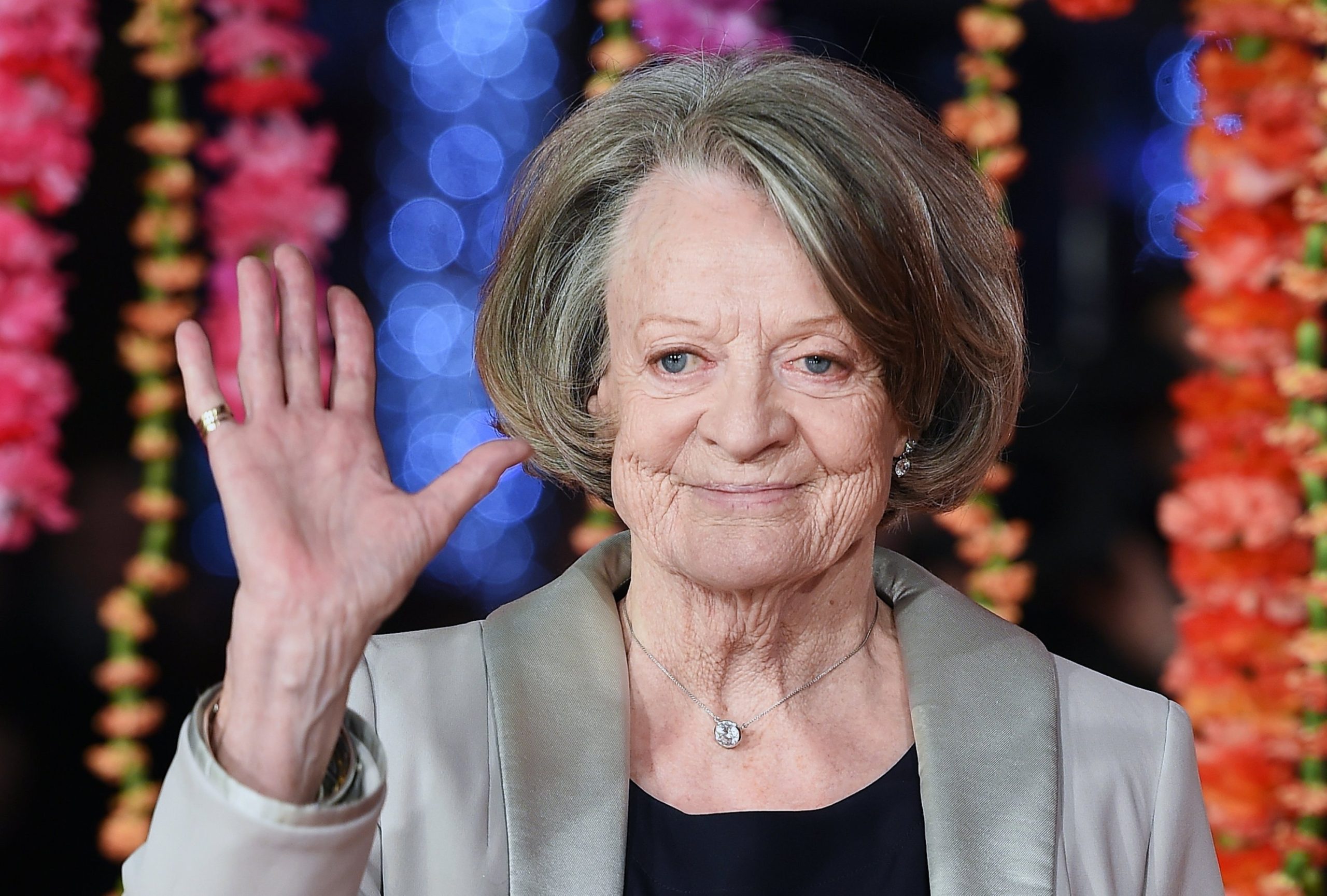 Dame Maggie Smith, elegantly aged, waving warmly to a crowd at a public event.