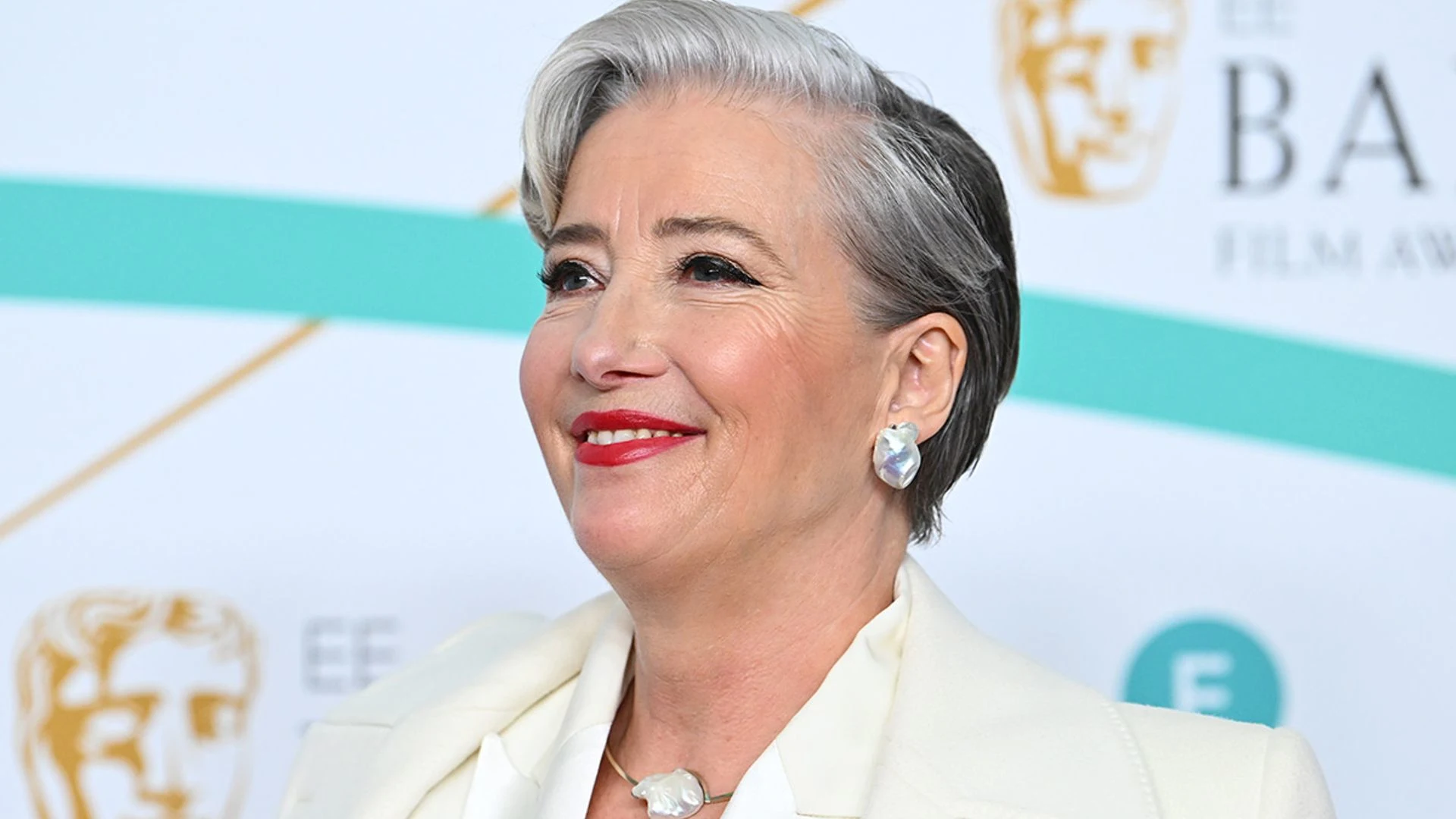 Emma Thompson dressed in a stunning white outfit, glammed up and posing elegantly on the BAFTA red carpet.