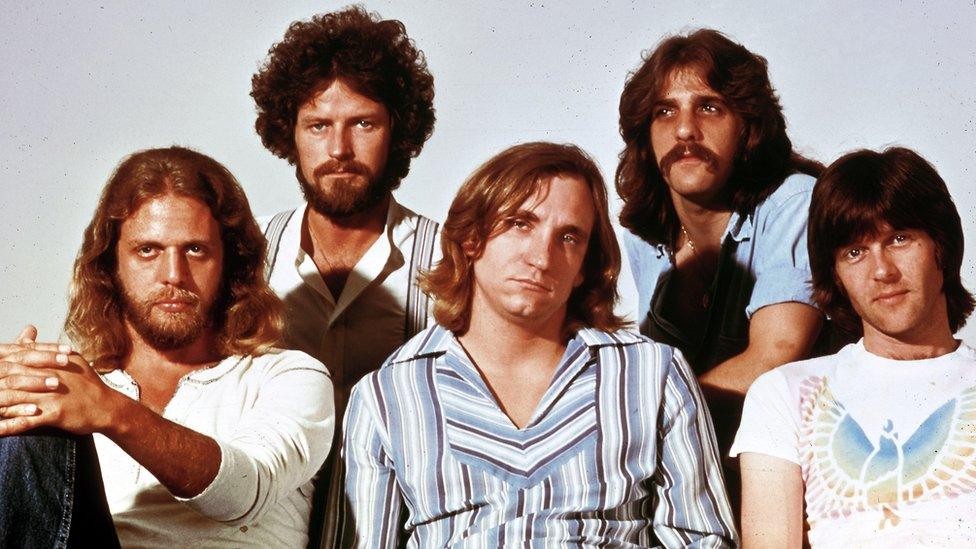 The Eagles band members sitting together, looking directly at the camera with serious expressions during a formal photo session.