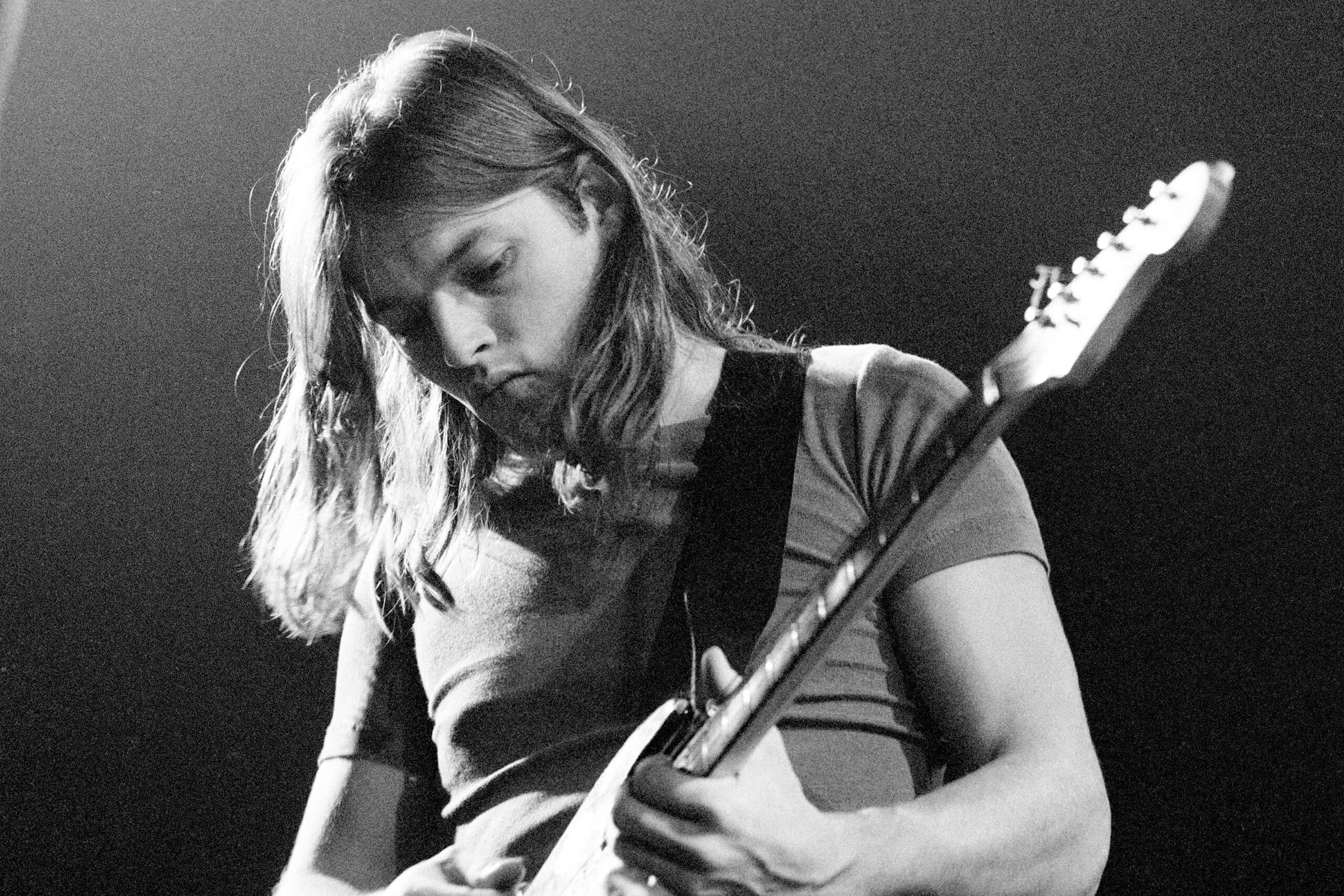 A young David Gilmour playing guitar in a black and white photo, focused and immersed in his performance.