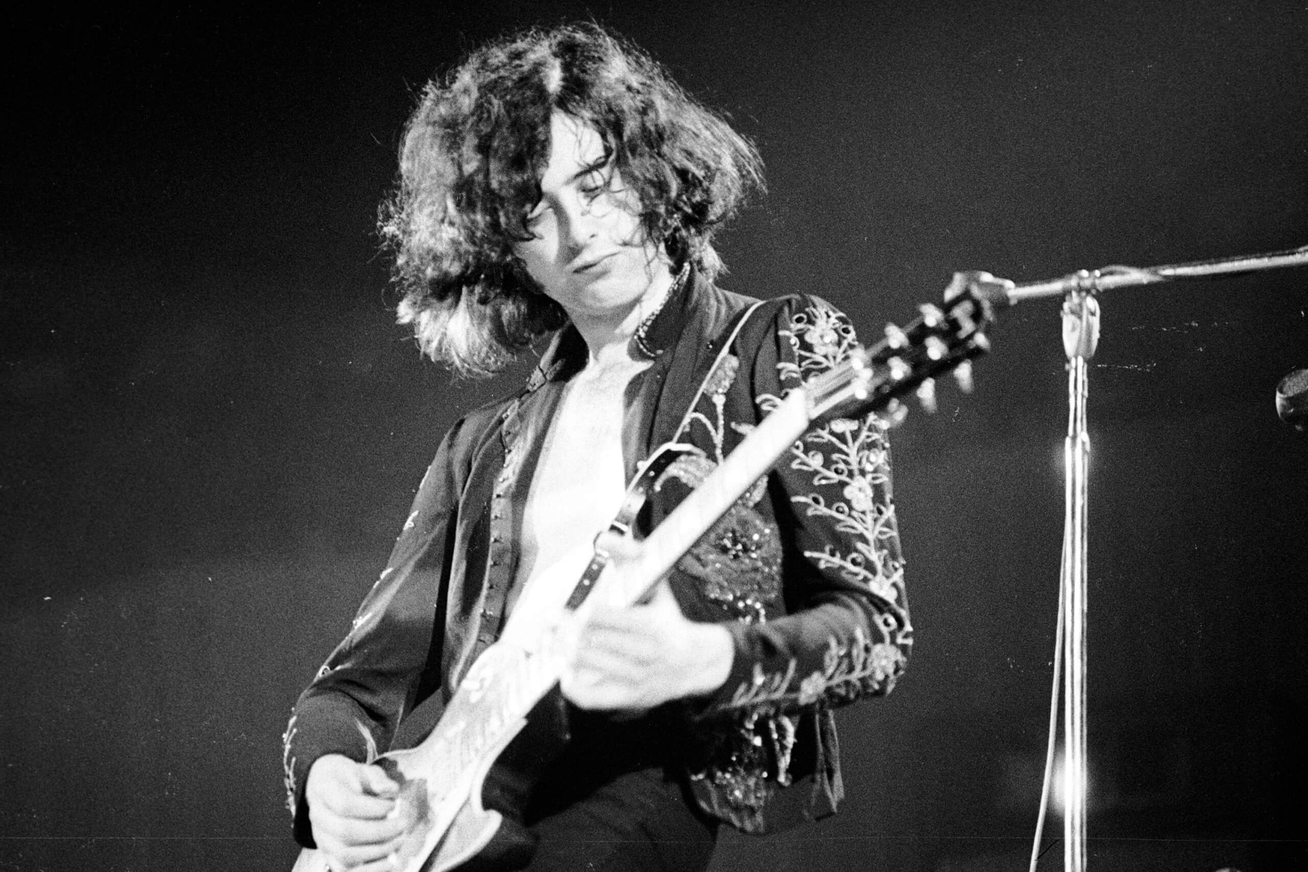 Young Jimmy Page passionately playing guitar on stage during a live rock performance, showcasing his signature energetic style.