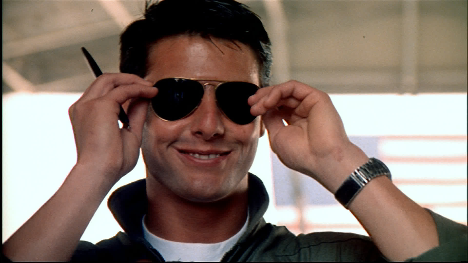 Tom Cruise smiling confidently while wearing sunglasses and a flight jacket in Top Gun.