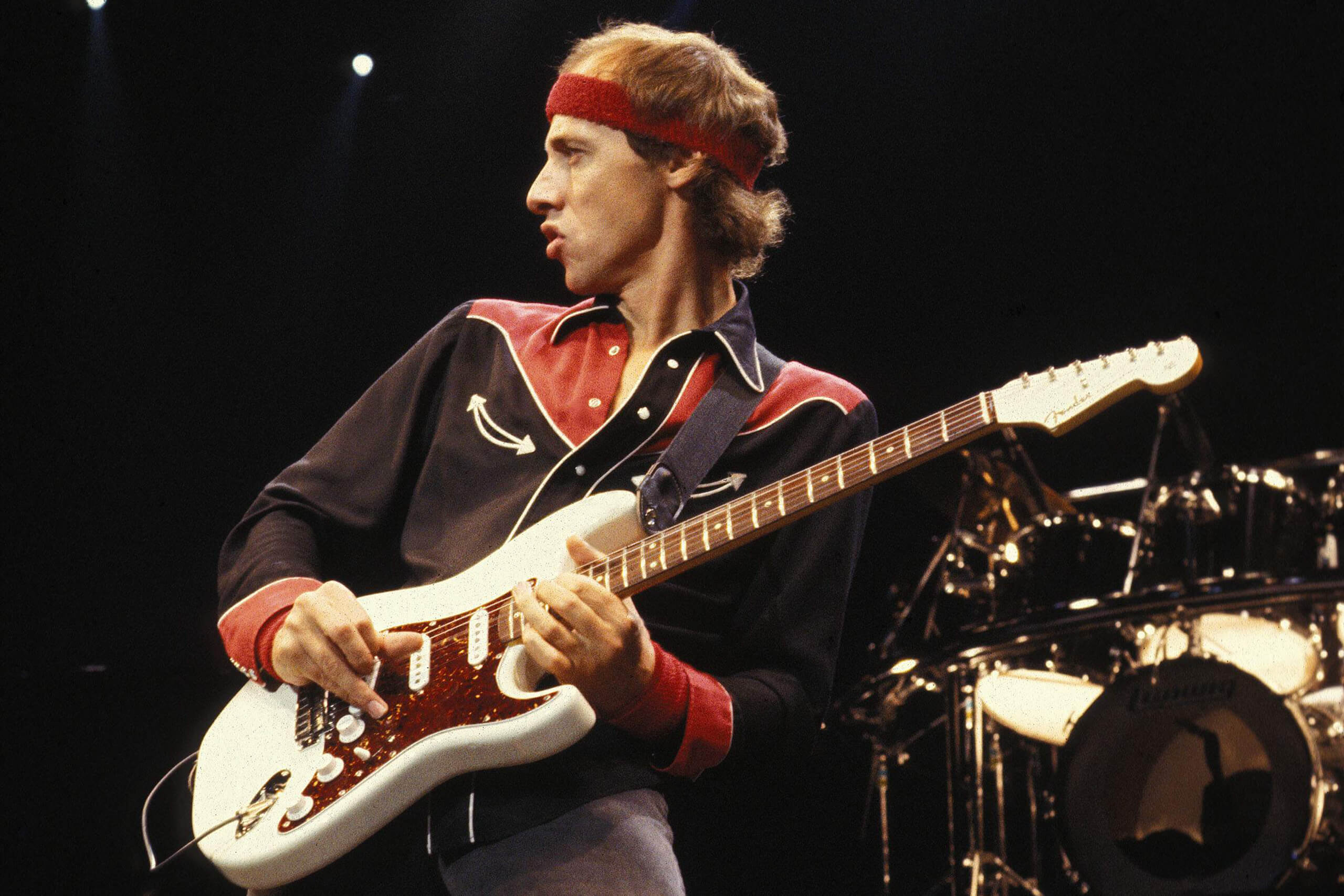 Mark Knopfler passionately playing guitar on stage during a live concert, immersed in his performance.