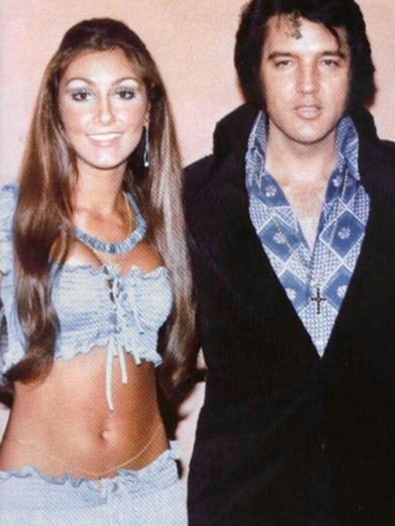 Elvis Presley with girlfriend Linda Thompson in a rare 1970s photo, both dressed in signature vintage fashion and posing closely together.