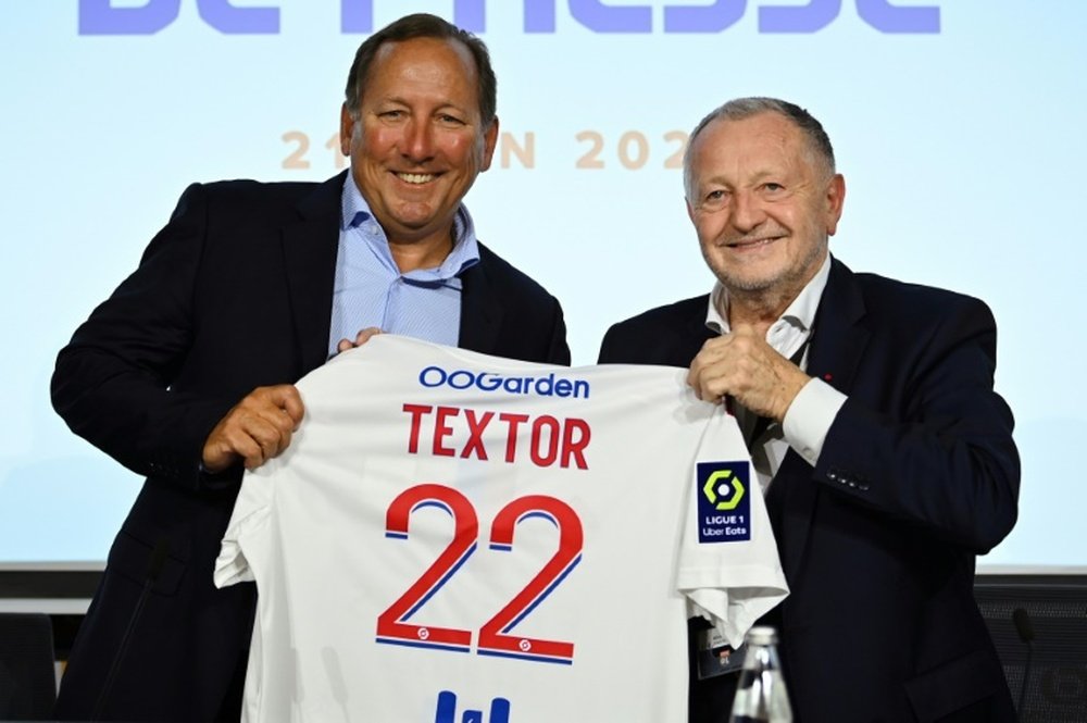 John Textor holding up an Olympique Lyonnais football shirt with "Textor 22" printed on the back.