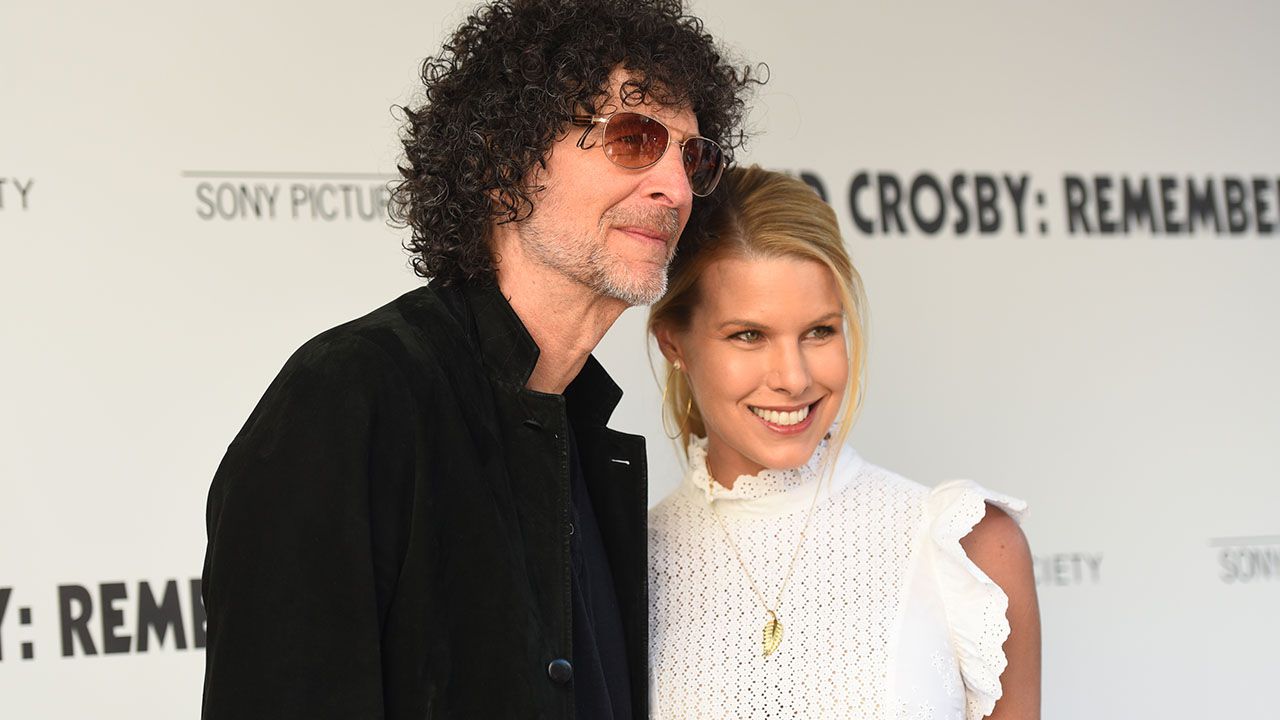 Howard Stern and his wife Beth Ostrosky Stern smile together on the red carpet, dressed elegantly and posing for photographers.