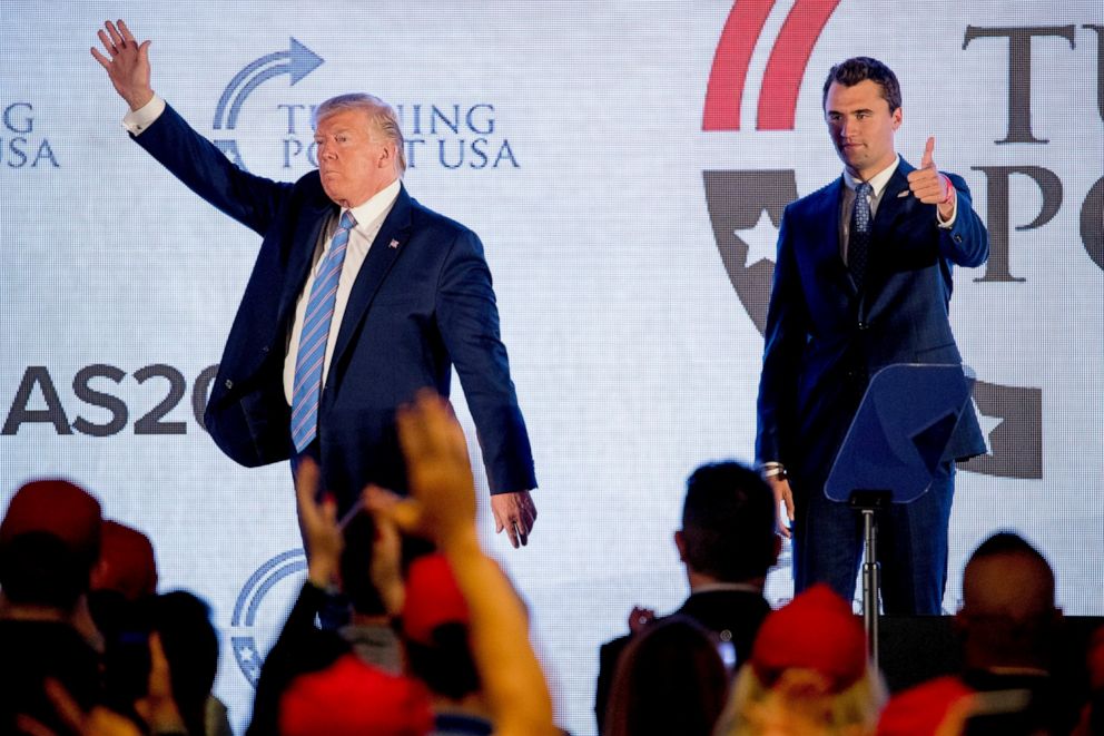 Charlie Kirk standing on stage next to Donald Trump, both waving to a cheering crowd.