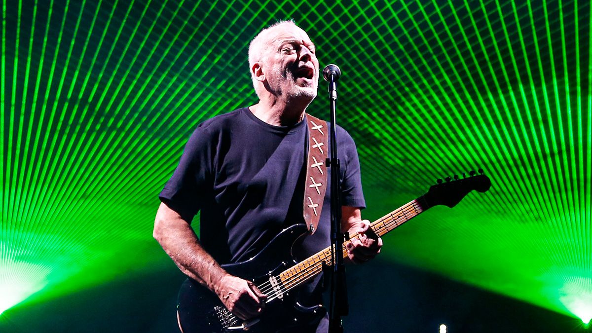 David Gilmour mid-performance on stage with intense neon green lights illuminating the background, passionately playing his guitar.