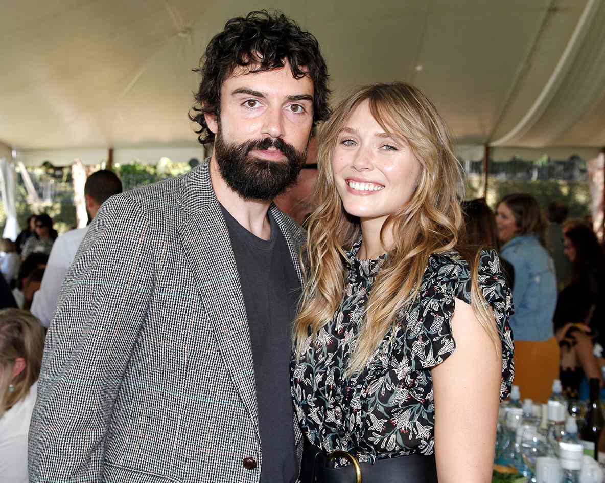 Elizabeth Olsen smiles warmly while standing next to her husband, Robbie Arnett, radiating happiness and togetherness.