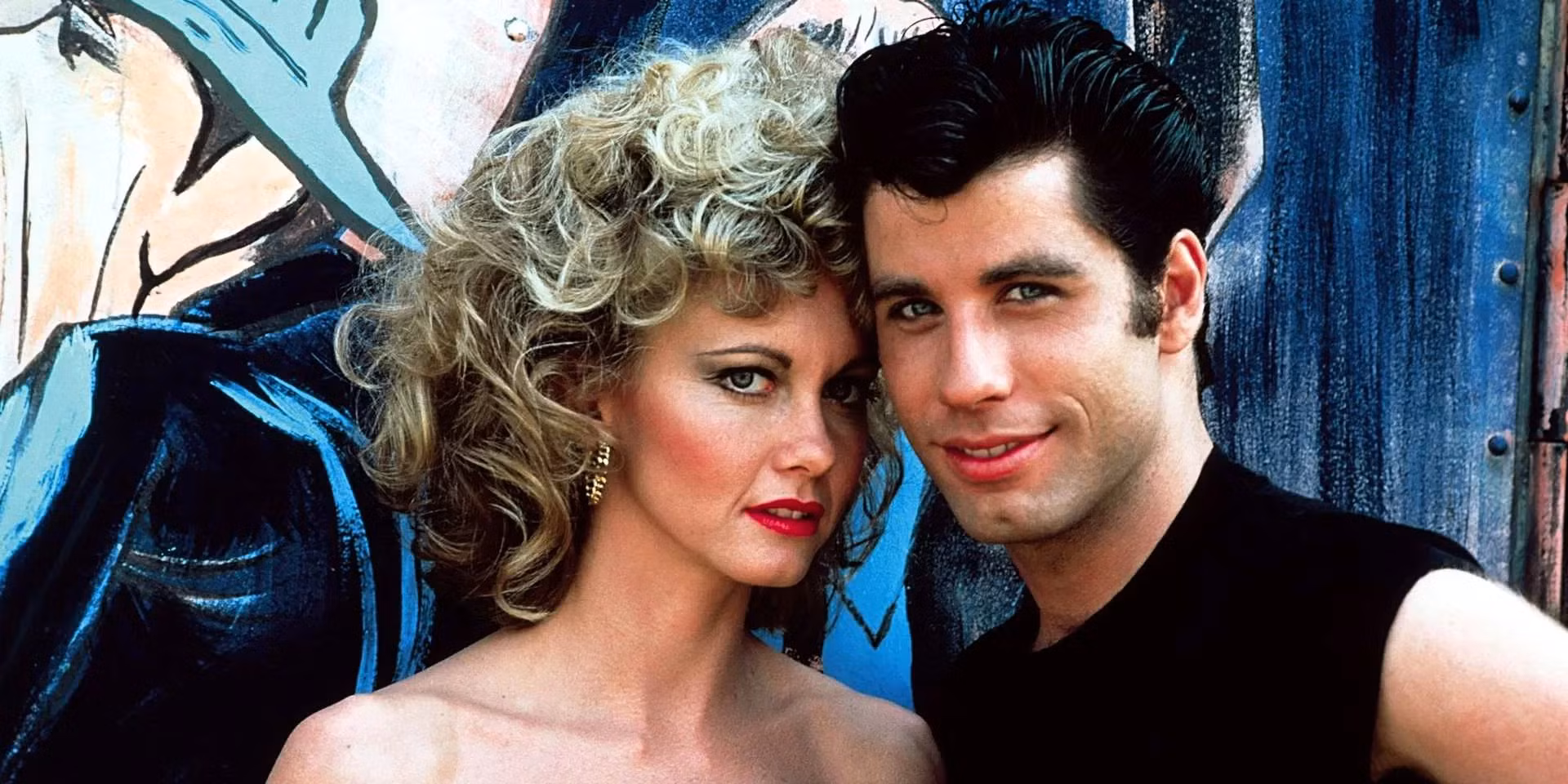 John Travolta and Olivia Newton-John smiling together on the set of Grease, dressed in their iconic 1950s-style costumes.