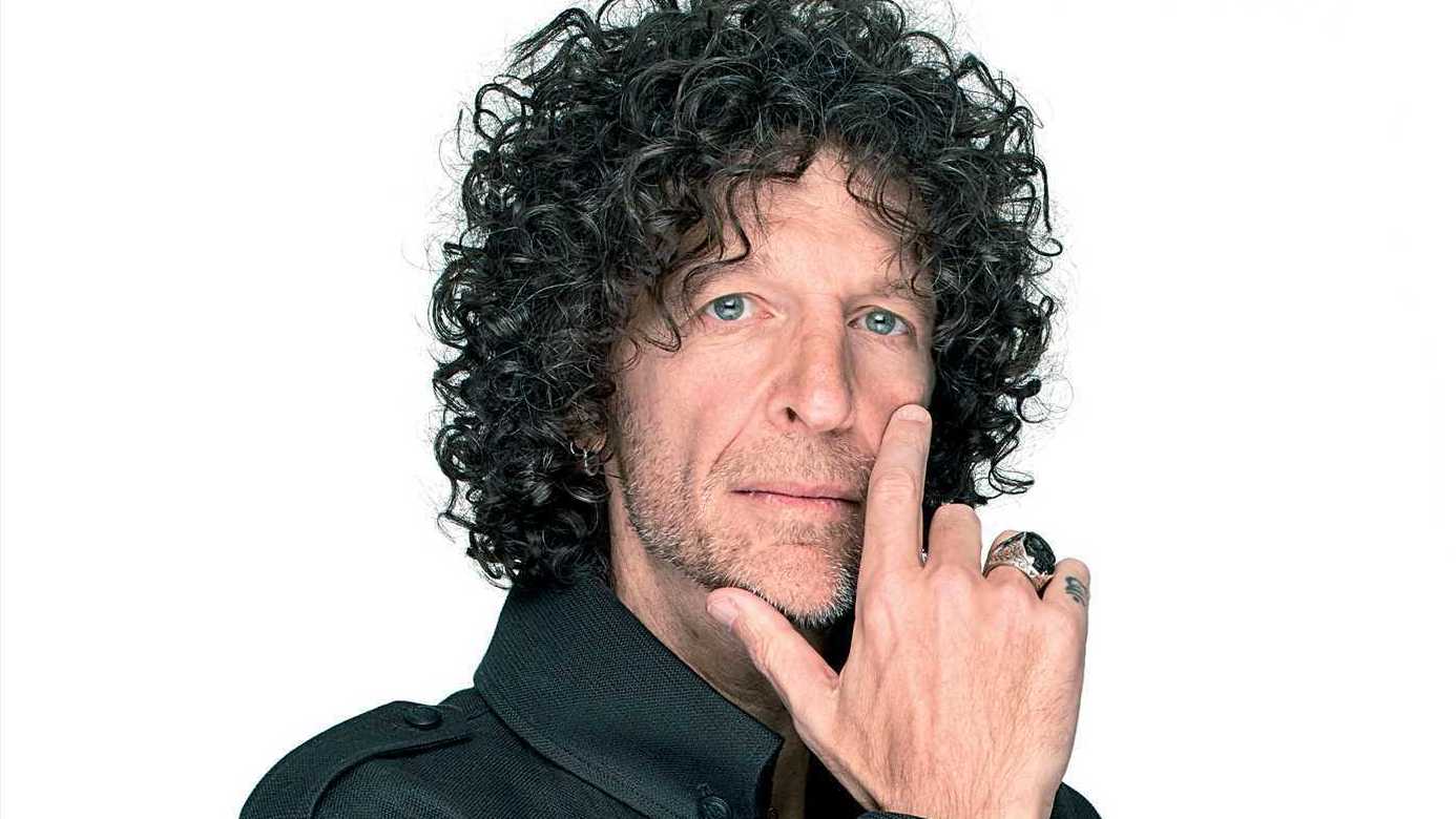 Howard Stern poses during a professional photoshoot, dressed in black with his signature curly hair and intense gaze directed at the camera.