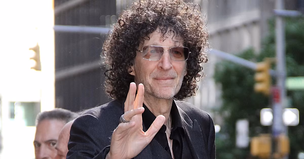 Howard Stern waves to fans gathered outside his studio, smiling and wearing sunglasses as he steps out to greet the crowd.