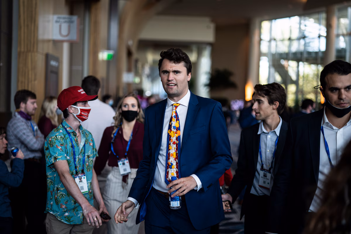 Charlie Kirk confidently walking down a university corridor wearing a suit.
