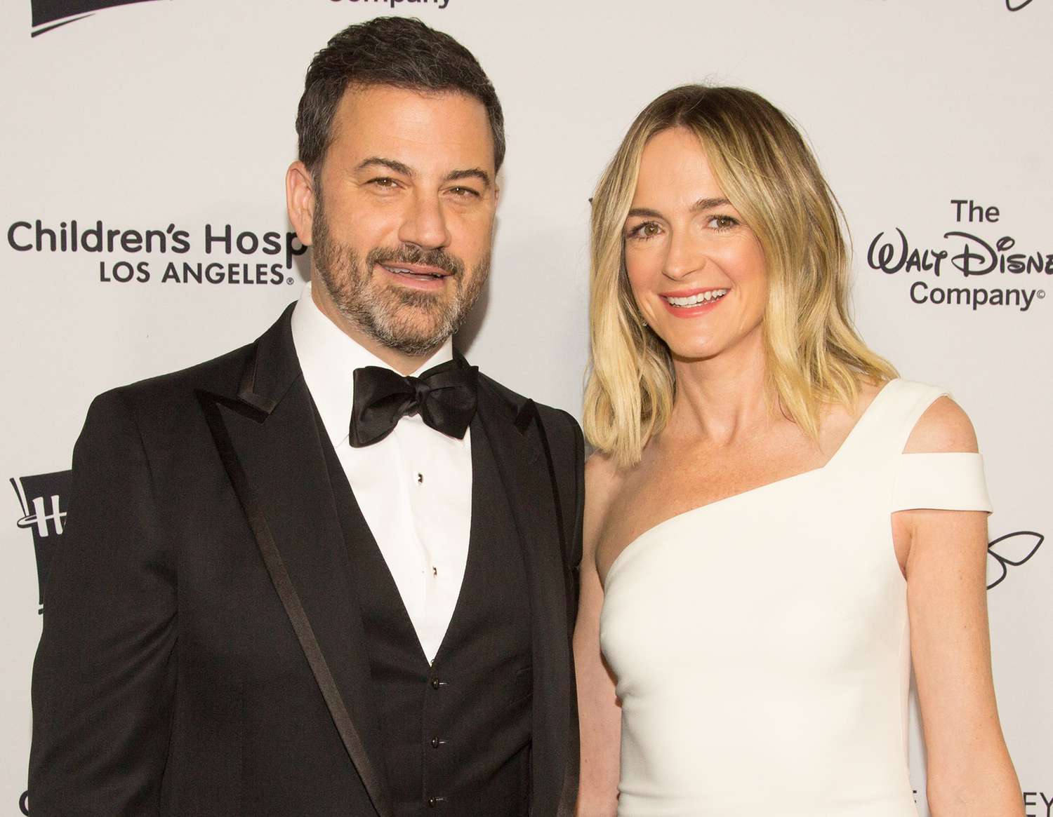 Jimmy Kimmel and his wife Molly McNearney pose together on the red carpet, dressed in elegant evening wear and smiling for the cameras.