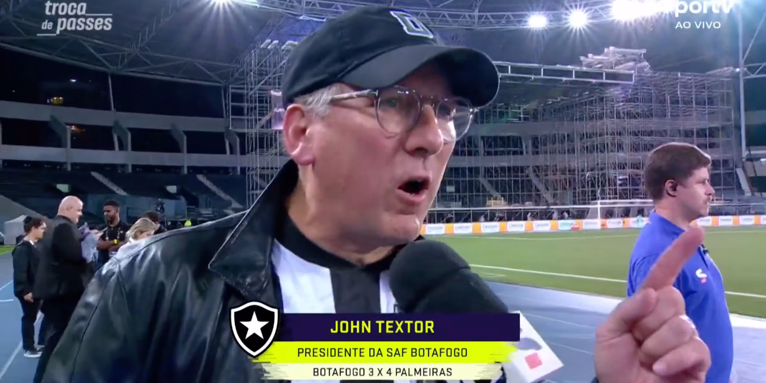 John Textor wearing a Botafogo football shirt, speaking during an interview with a focused expression.