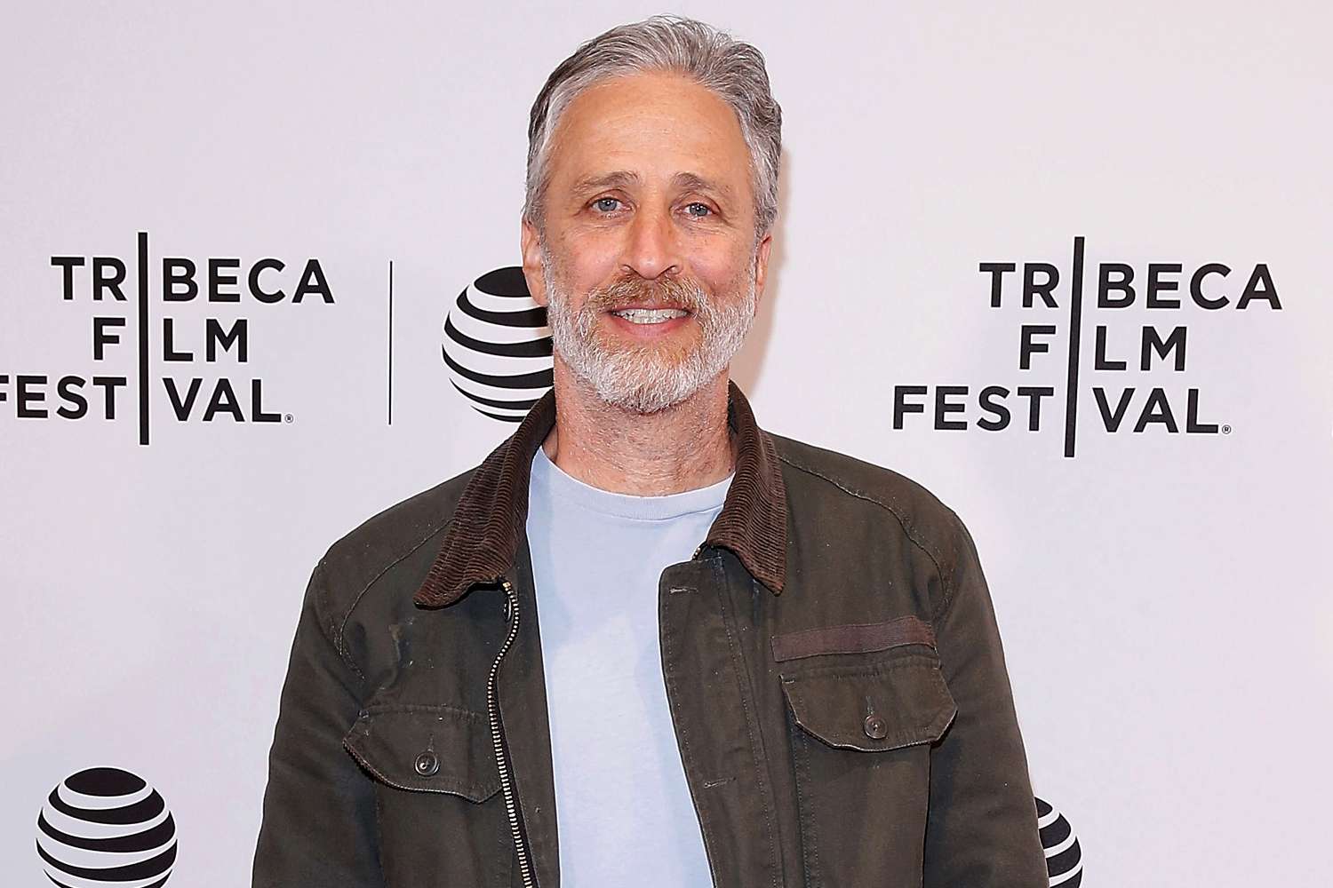 Jon Stewart walks the red carpet at the Tribeca Film Festival, dressed in a tailored suit and smiling for the cameras.