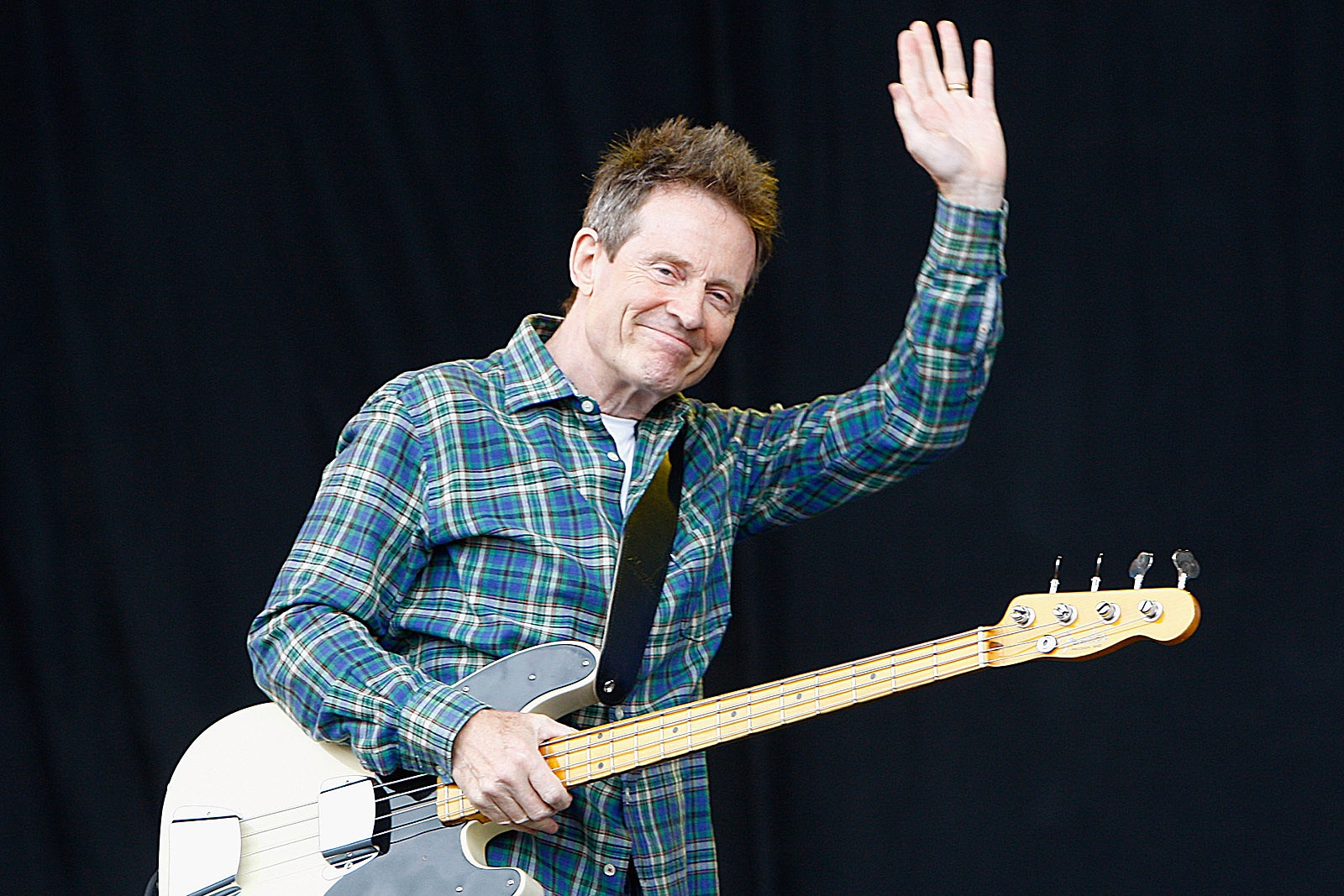 John Paul Jones waving to an enthusiastic crowd during a live concert, illuminated by stage lights.