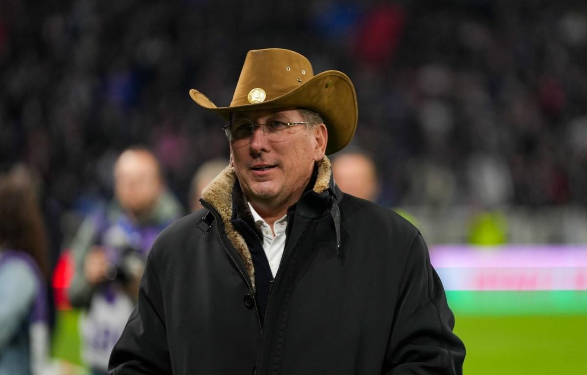 John Textor stands on a football pitch wearing a cowboy hat, exuding confidence and charisma.