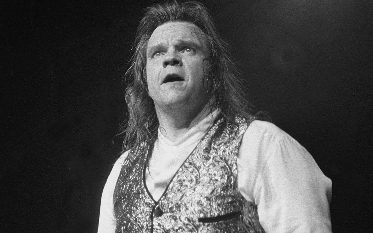 Black and white photo of Meat Loaf mid-performance, mouth open passionately as he looks out at the crowd.