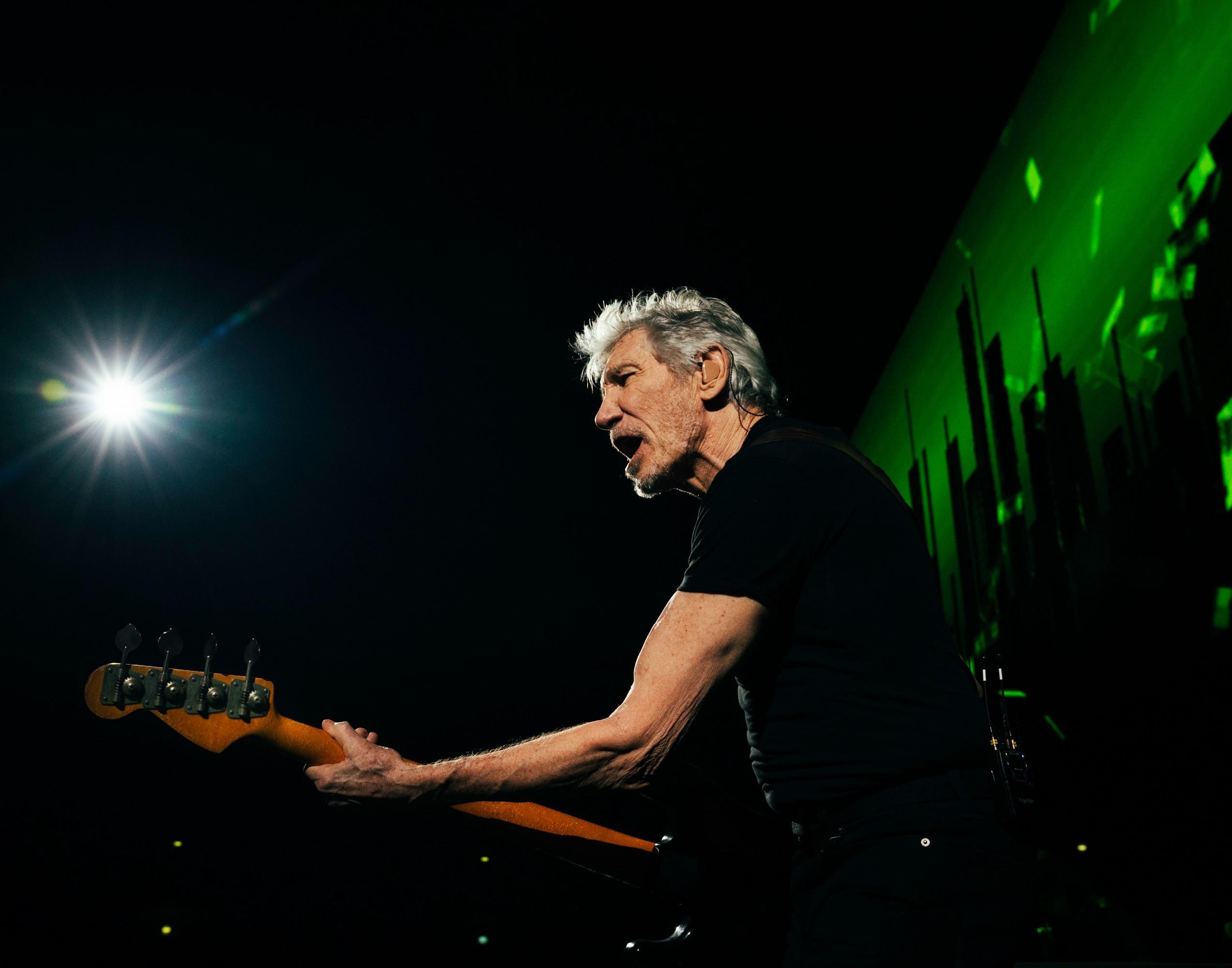 Roger Waters mid-performance on stage, mouth open passionately as he sings with intensity.