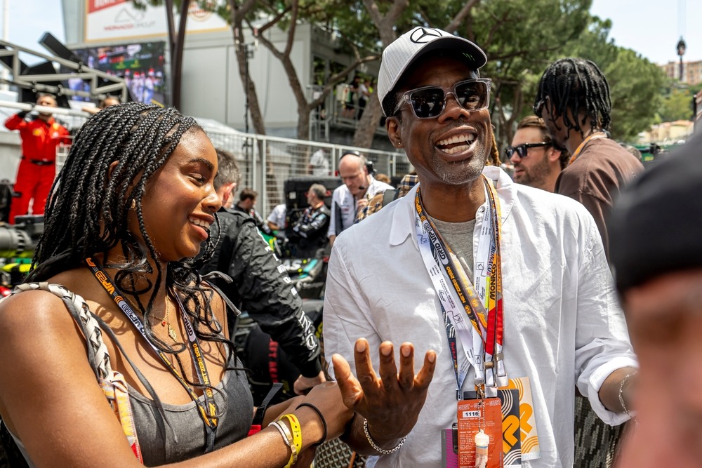 Chris Rock attending a Formula 1 Grand Prix event, wearing sunglasses and a team cap in the paddock.