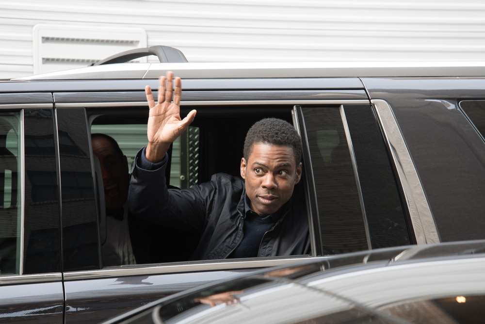Chris Rock waves from the window of a black limousine, smiling at fans during a public appearance.