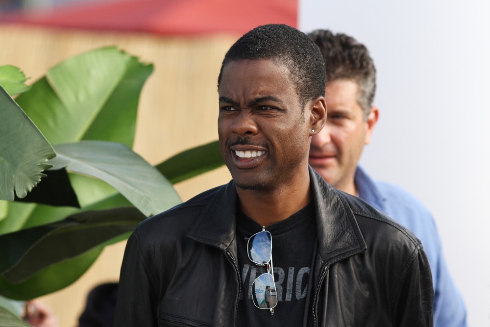 Chris Rock pulls a confused, animated expression while wearing a black leather jacket during a live performance.