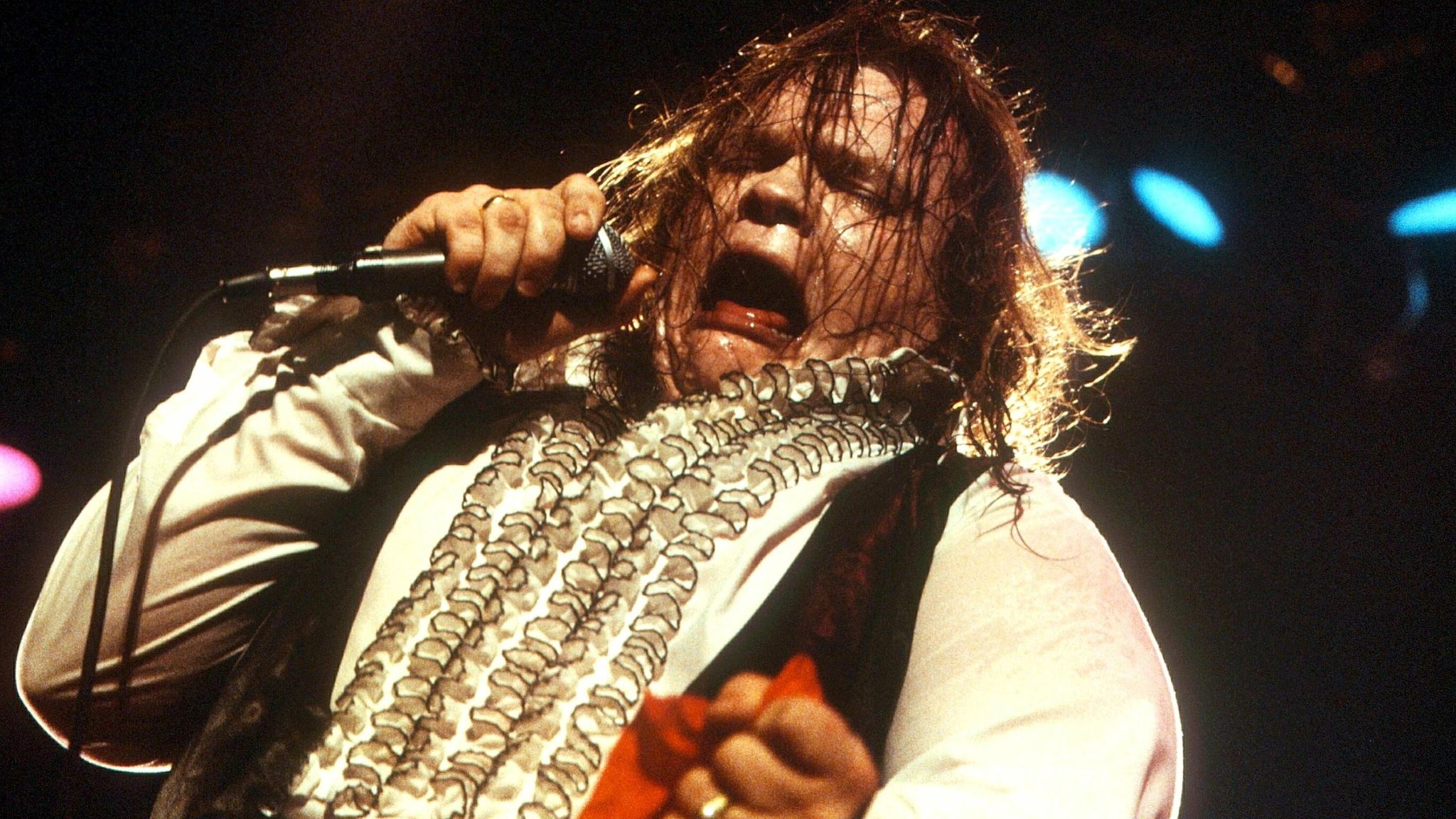 Meat Loaf performing intensely on stage, drenched in sweat, passionately singing and giving an electrifying performance.