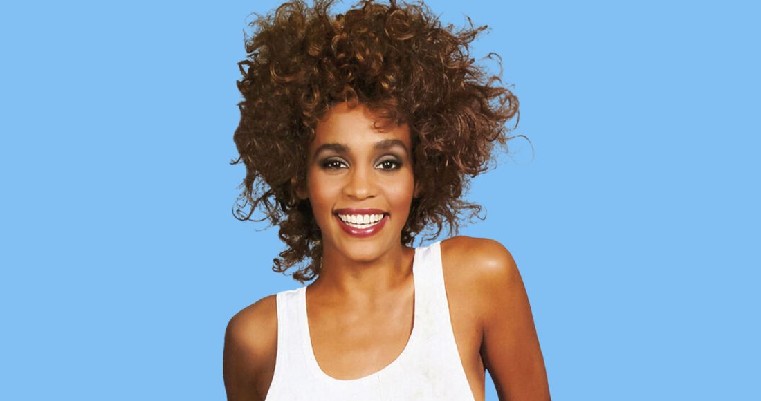 Whitney Houston smiling in a white tank top against a bright blue background, with her curly hair styled voluminously.